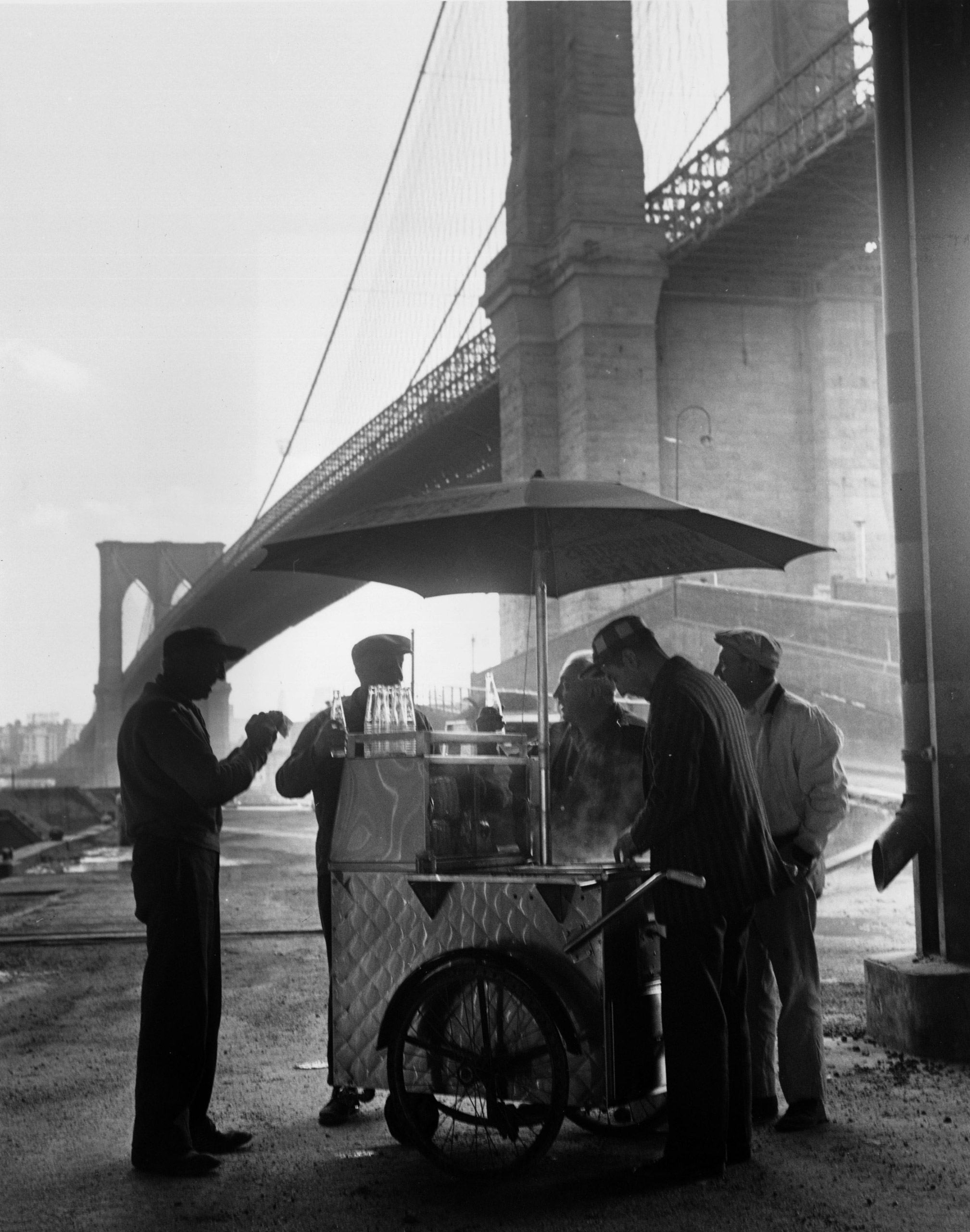 A group of workers getting refreshments from a portable snack stand underneath Brooklyn Bridge.