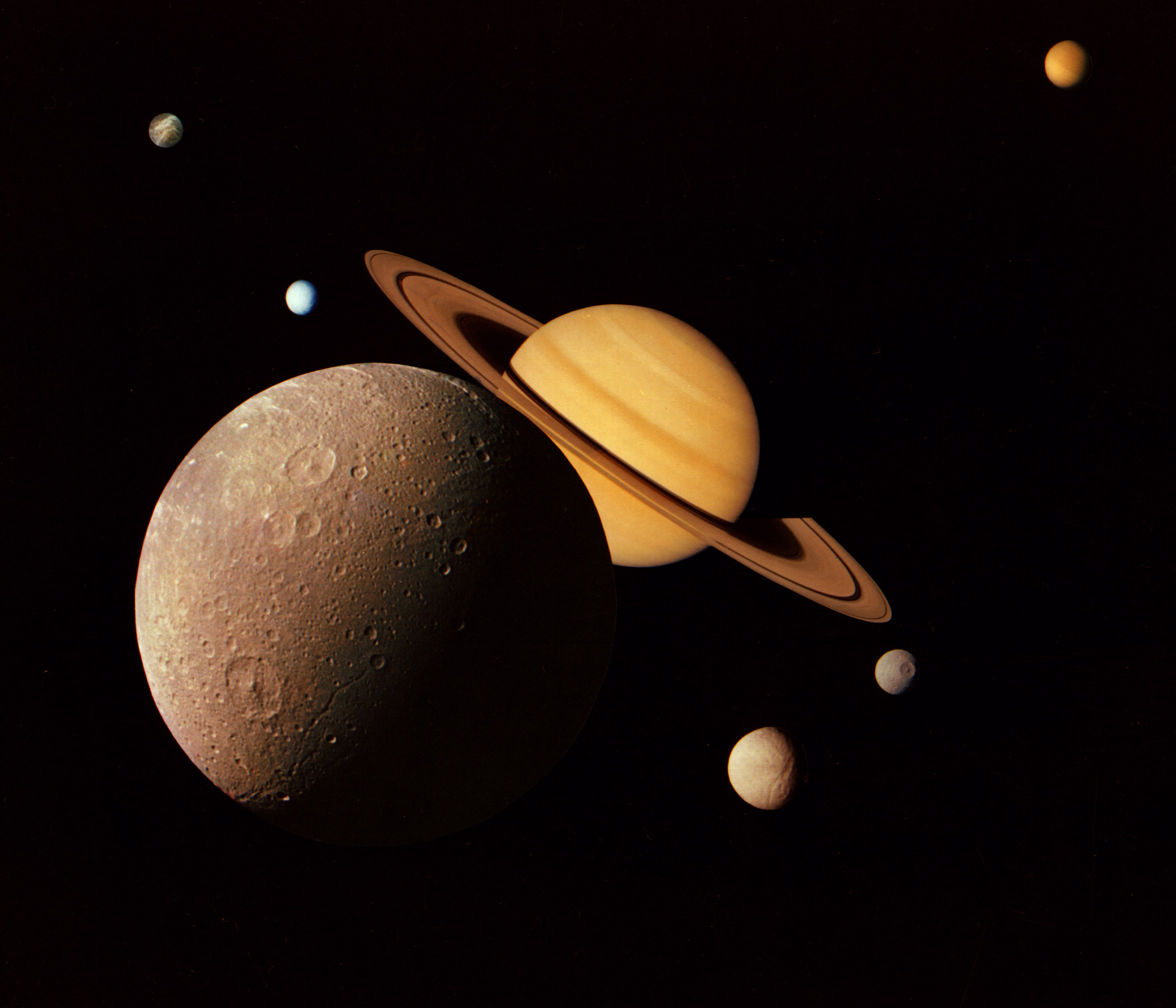 This montage of images of the Saturnian system was prepared from an assemblage of images taken by the Voyager 1 spacecraft during its Saturn encounter in November 1980. This artist's view shows Dione in the forefront, Saturn rising behind, Tethys and Mimas fading in the distance to the right, Enceladus and Rhea off Saturn's rings to the left, and Titan in its distant orbit at the top. The Voyager Project is managed for NASA by the Jet Propulsion Laboratory, Pasadena, California.