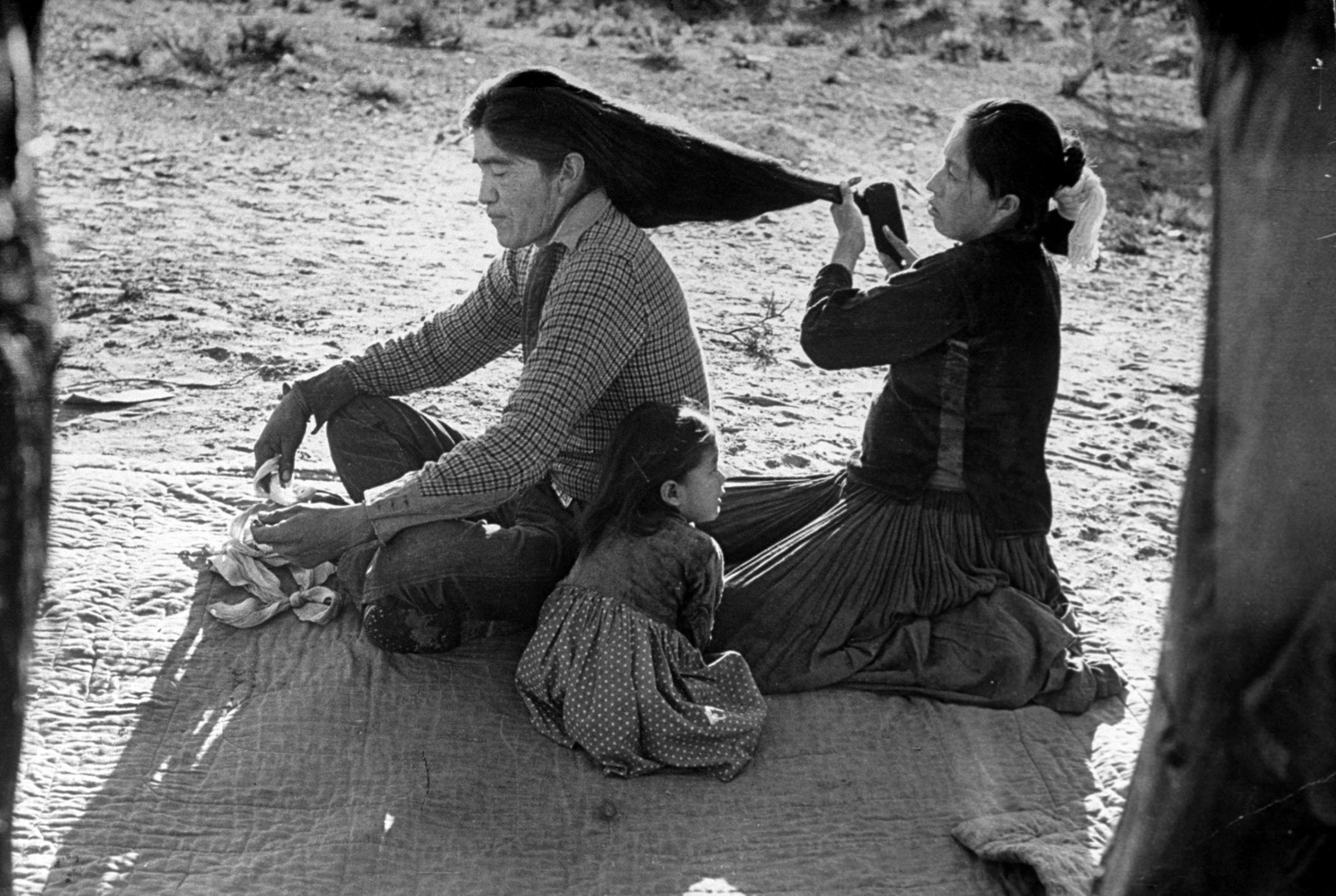 Yellowsalt's son has his hair brushed by wife. Nowadays many young Navajos wear their hair short.