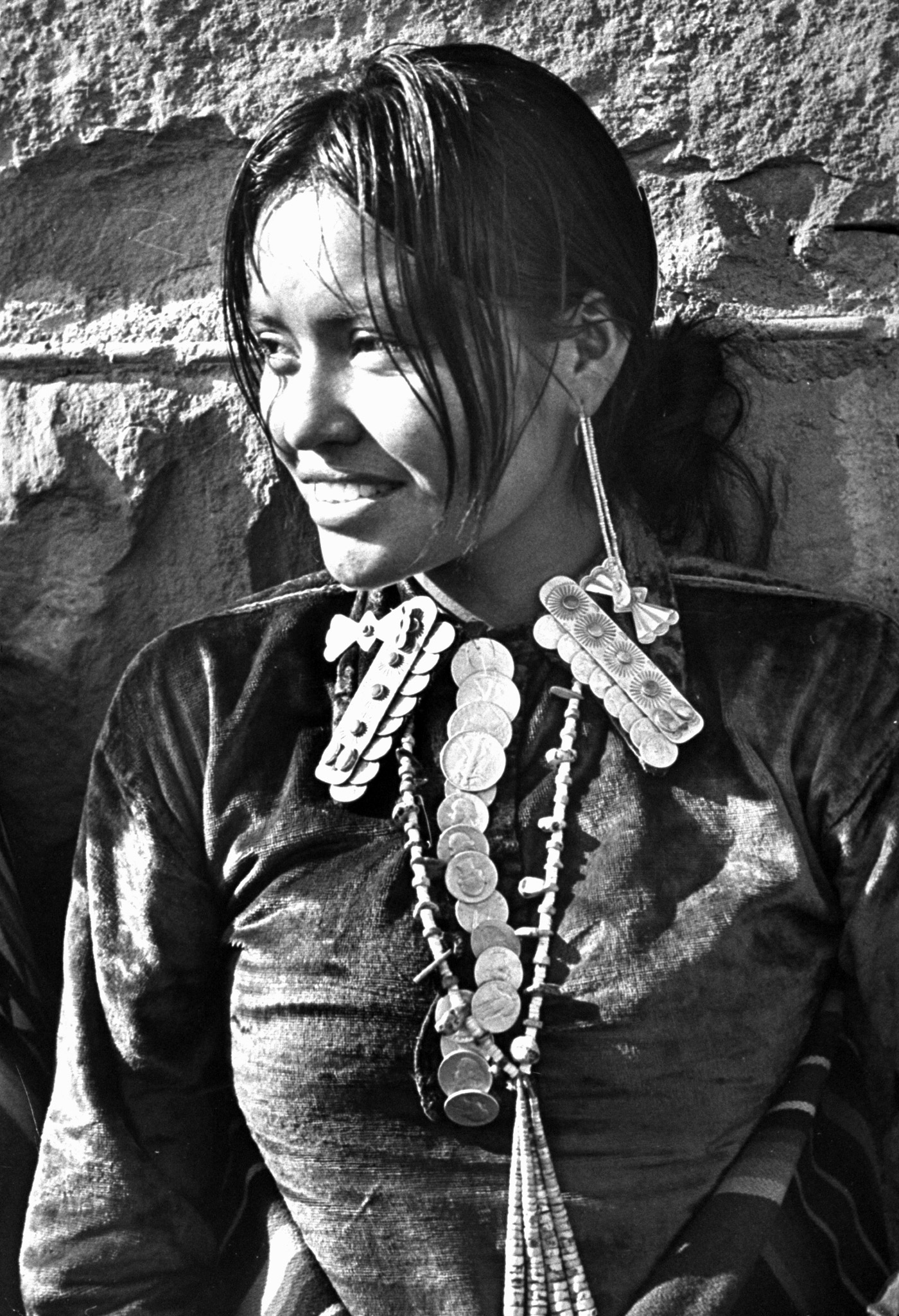 Navajo woman sporting Navajo-crafted silver shirt collar caps, long beaded earrings, beaded necklace complete with silver quarters and 50 cent pieces strung together like a tie.