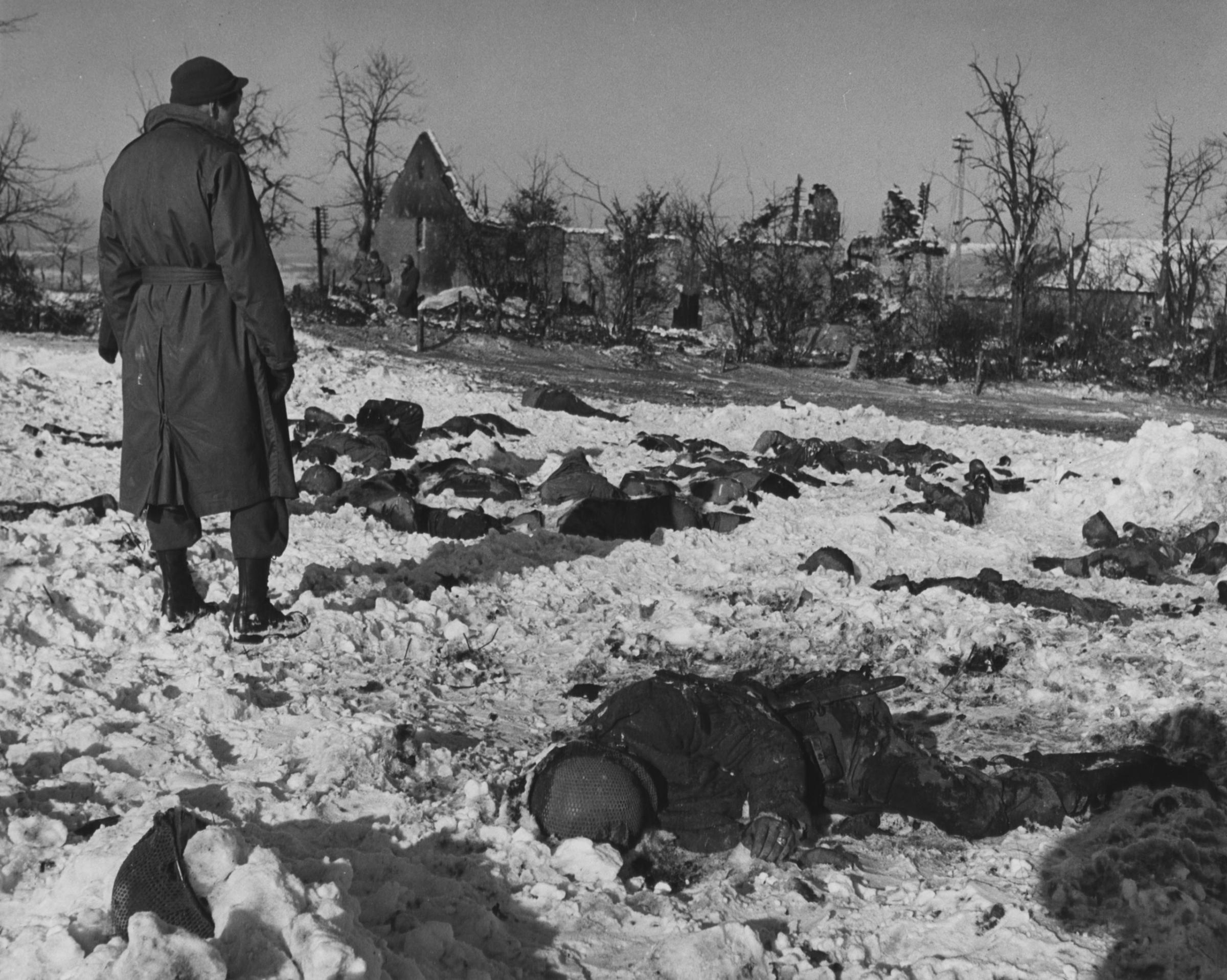 An American Soldier Looks Numbly at Bodies of American Prisoners Who Were Shot by the Germans, near Malmedy, Belgium. 84 American Prisoners of War Were Murdered during the Malmedy Massacre, December 17, 1944