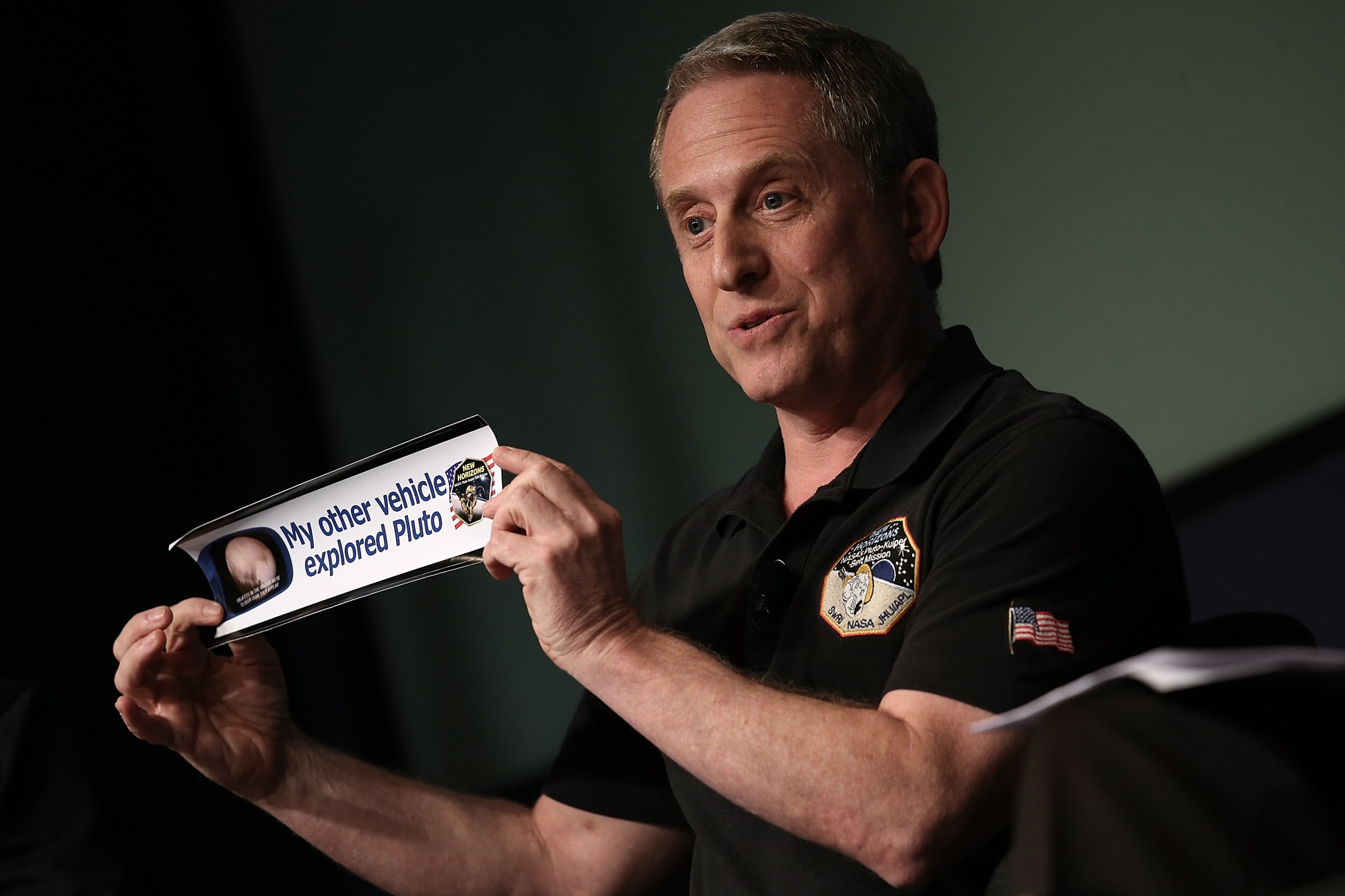 Alan Stern, principal investigator of NASA's New Horizons mission team, holds up a bumper sticker while delivering remarks during a press briefing at NASA headquarters in Washington, DC on July 24, 2015.