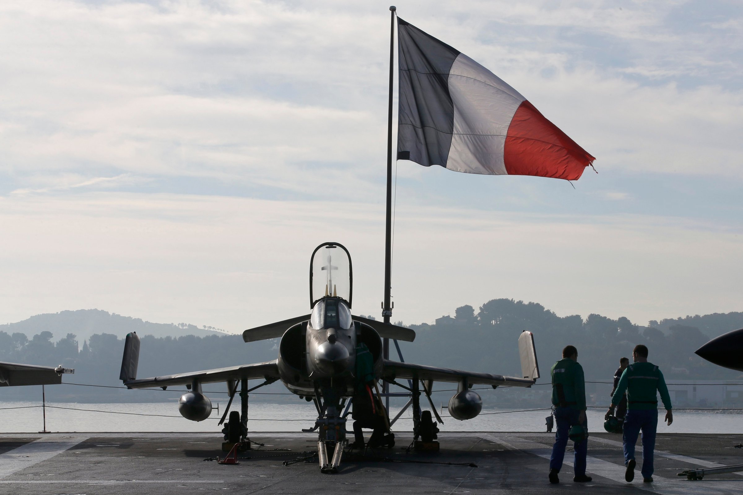 Flight deck crew work around a Super Etendard fighter jet as a French flag flies aboard the French nuclear-powered aircraft carrier Charles de Gaulle before its departure from the naval base of Toulon