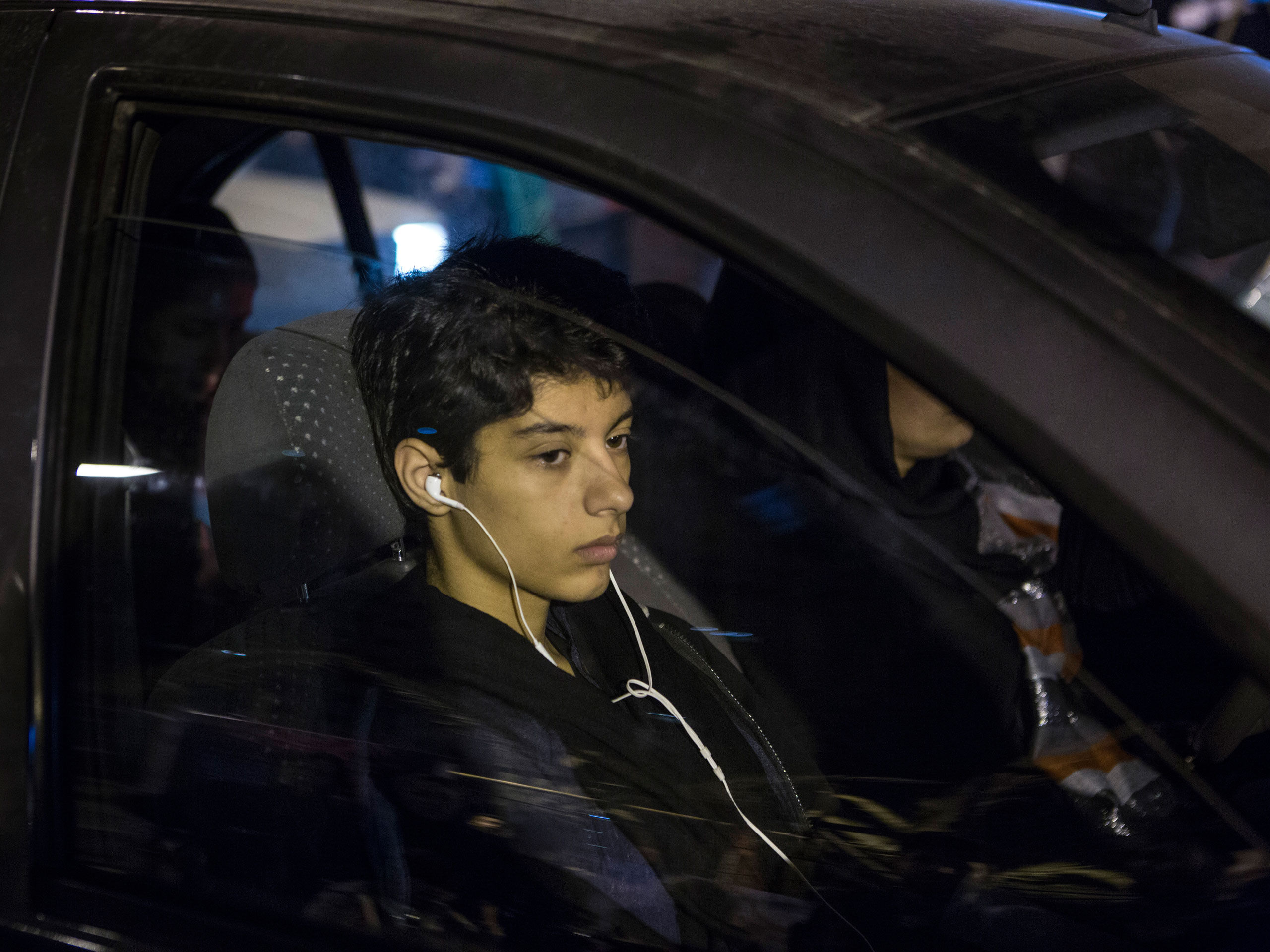 A young man sits in a car next to his mother in Tehran, where the use of headsets and mobile phones is widespread.