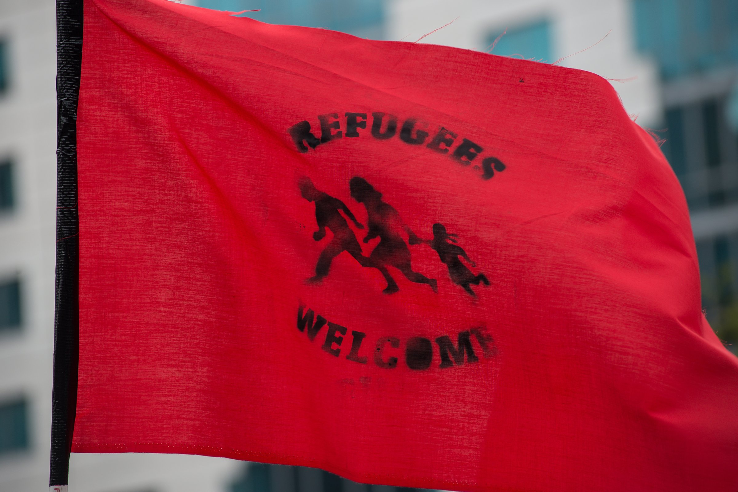 A demonstrator holds a flag declaring "Refugees Welcome." A