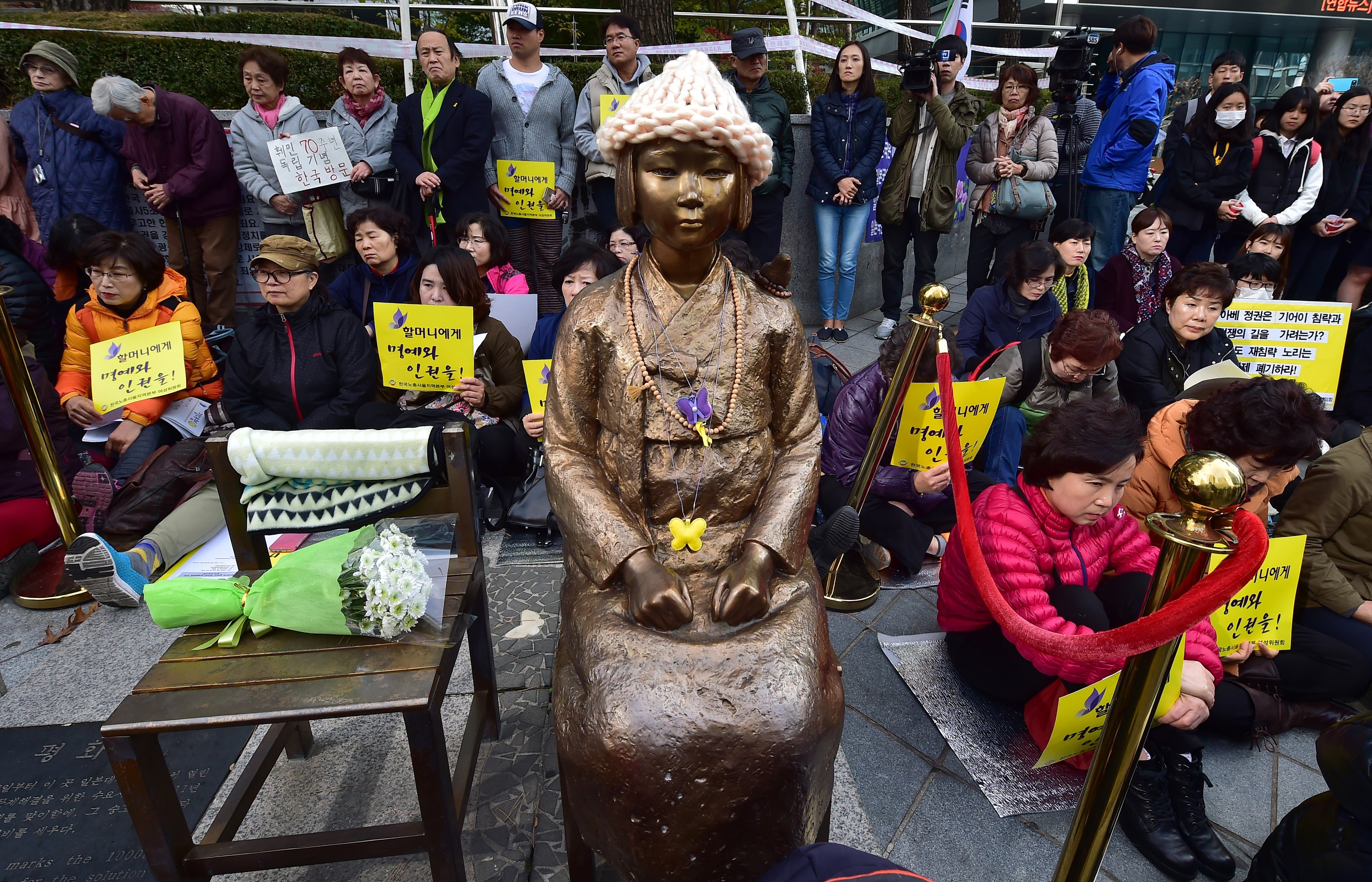 Protesters sit next to a statue of a South Korean teenage girl, center, during a weekly anti-Japanese demonstration near the Japanese embassy in Seoul on Nov. 11, 2015 (Jung Yeon-Je—AFP/Getty Images)