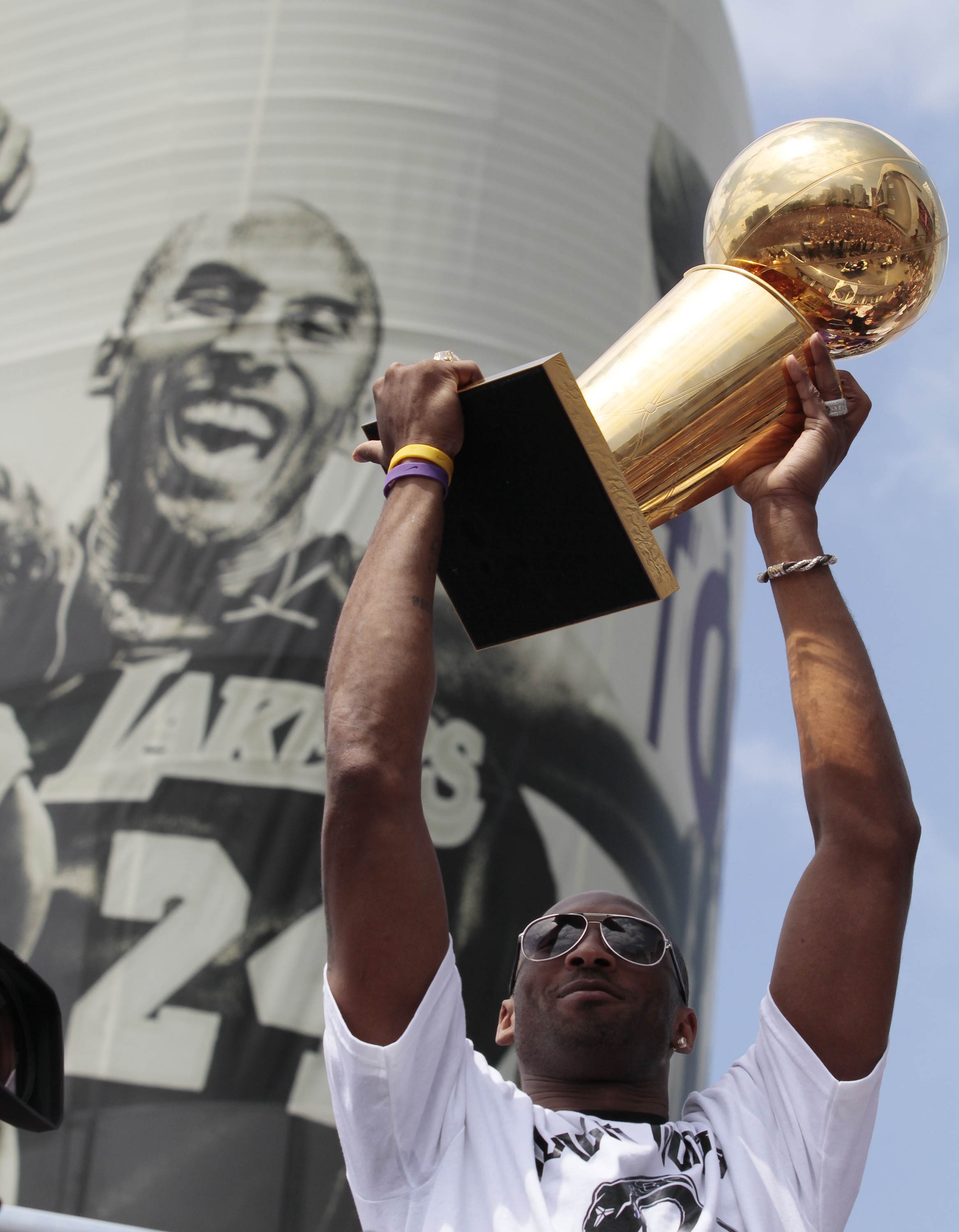 Kobe Bryant raises the NBA championship trophy in front of a poster of himself on the Staples Center during a victory parade for the teams 16th NBA title in Los Angeles on June 21, 2010. His fifth and final title, following a hard-fought seven-game Finals against the Boston Celtics, was — in his words — the most satisfying of them all.