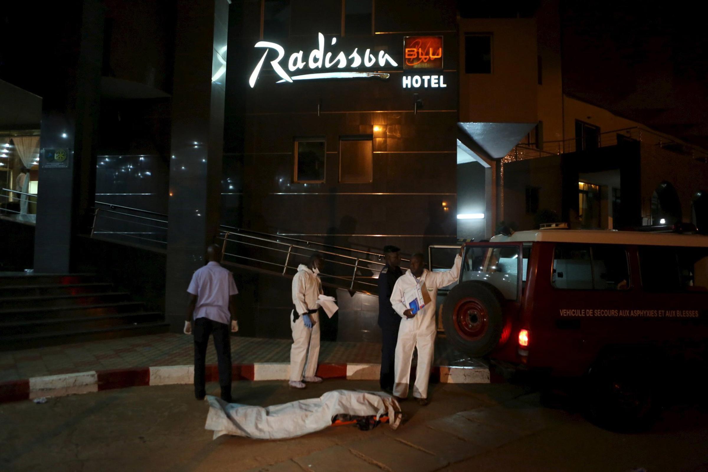Malian officials prepare to lift a corpse into an emergency vehicle outside the Radisson hotel in Bamako