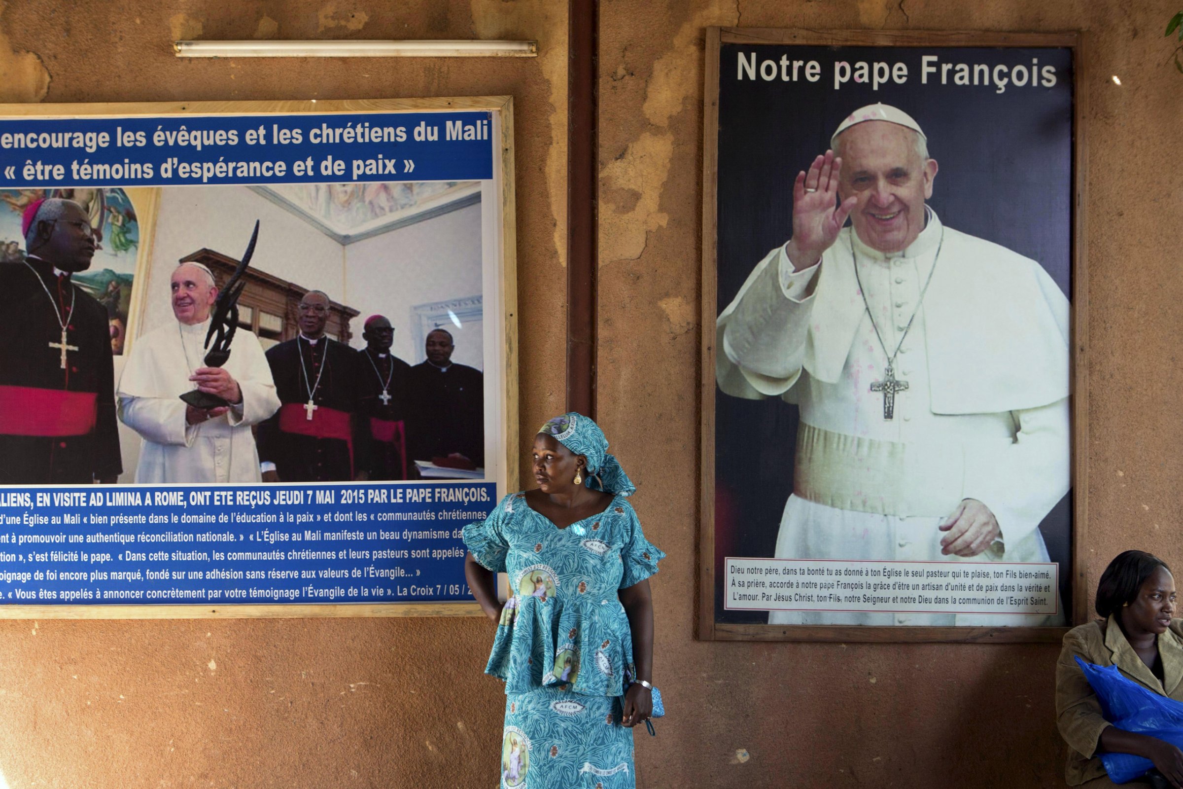 A woman stands in front of posters of Pope Francis at the Martyrs of Uganda church in Bamako, Mali, November 8, 2015. The poster on the right reads, "Our Pope Francis". Pope Francis makes his first pontifical visit later this month to Africa, where Catholicism has grown rapidly over the last few decades but now faces serious competition from Evangelical and Pentecostal churches, as well as Islam. The pontiff's trip to Africa, where an estimated 1 in 5 people is Catholic, takes in Kenya, Uganda and Central African Republic. His visit to that country is fraught with security concerns after months of clashes between Christians and Muslim gangs in which dozens of people have been killed. REUTERS/Joe PenneyPICTURE 6 OF 13 FOR WIDER IMAGE STORY "CATHOLICISM IN AFRICA". SEARCH "PONTIFF EVANGELICAL" FOR ALL IMAGES - RTS82NC