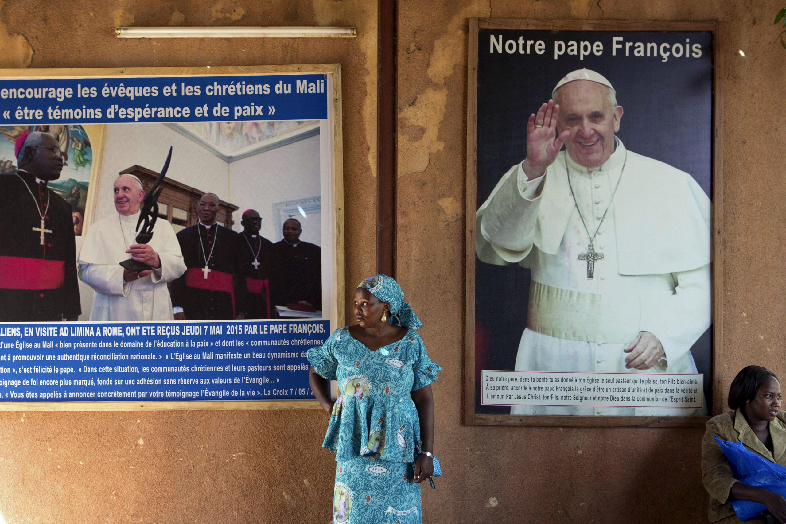 A woman stands in front of posters of Pope Francis at the Martyrs of Uganda church in Bamako, Mali, November 8, 2015. The poster on the right reads, "Our Pope Francis". Pope Francis makes his first pontifical visit later this month to Africa, where Catholicism has grown rapidly over the last few decades but now faces serious competition from Evangelical and Pentecostal churches, as well as Islam. The pontiff's trip to Africa, where an estimated 1 in 5 people is Catholic, takes in Kenya, Uganda and Central African Republic. His visit to that country is fraught with security concerns after months of clashes between Christians and Muslim gangs in which dozens of people have been killed.  REUTERS/Joe PenneyPICTURE 6 OF 13 FOR WIDER IMAGE STORY "CATHOLICISM IN AFRICA". SEARCH "PONTIFF EVANGELICAL" FOR ALL IMAGES   - RTS82NC