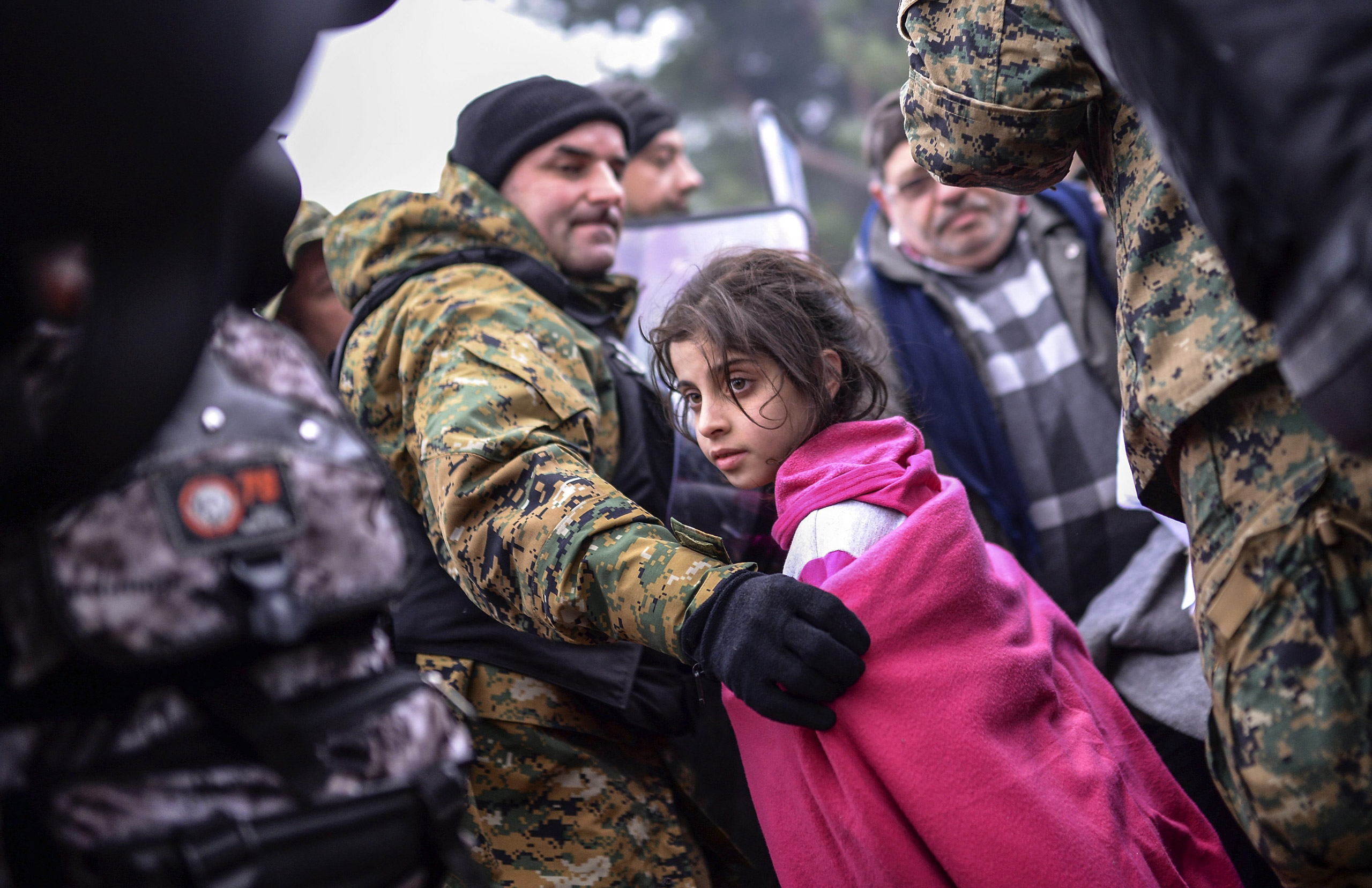 A Macedonian police officer helps a girl move past the cordon on the Greek-Macedonian border after Macedonia has started letting in refugees from Syria, Iraq and Afghanistan, near Gevegelija, Macedonia, on 20 Nov. 2015. (Georgi Licovski—EPA)