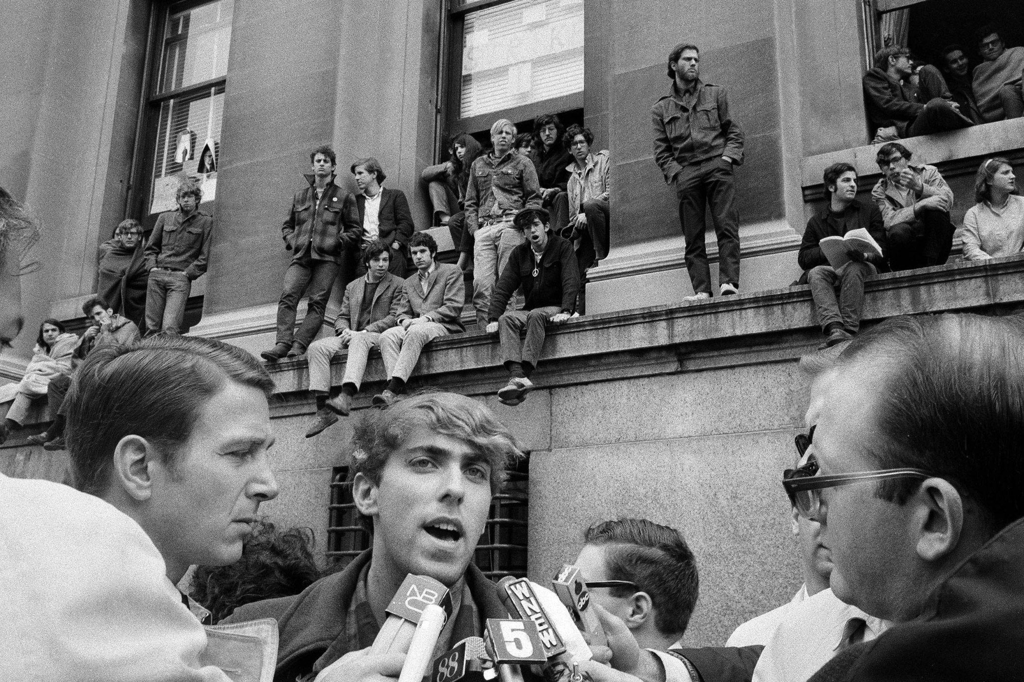 Mark Rudd, a leader of the student protest at Columbia University in New York, speaks to reporters as fellow students, rear, occupy the Low Memorial Library on April 25, 1968. Standing on ledge, center, with hands in pockets, is Juan Gonzalez, another of the student leaders. The 1968 Columbia University Protests targeted a variety of issues, most notably the Vietnam War.