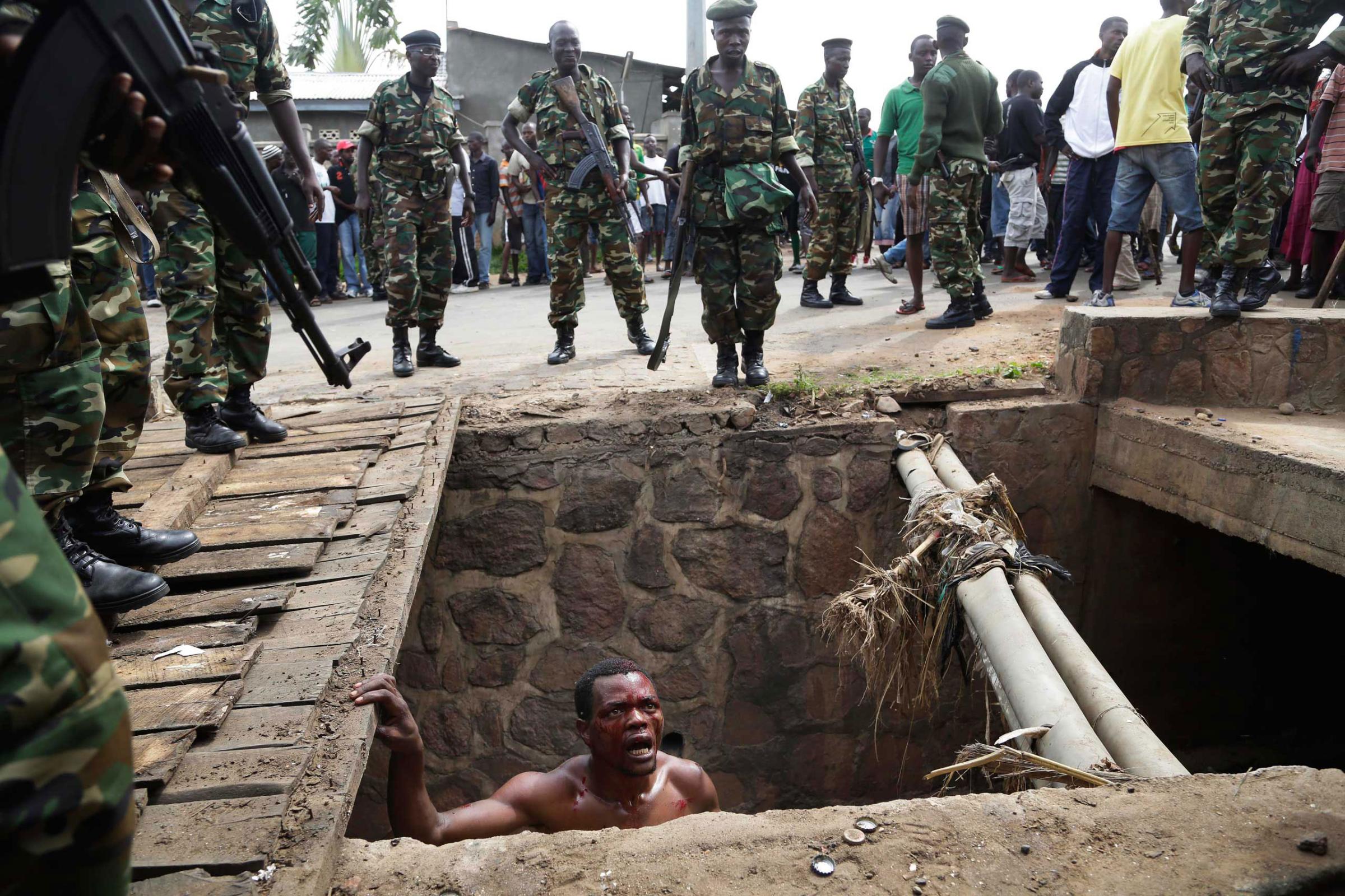 Jean Claude Niyonzima, a suspected member of the ruling party's Imbonerakure youth militia, pleads with soldiers to protect him from a mob of demonstrators after he emerged from hiding in a sewer in the Cibitoke district of Bujumbura, Burundi. Niyonzima escaped the lynching by running into the sewer. May 7, 2015