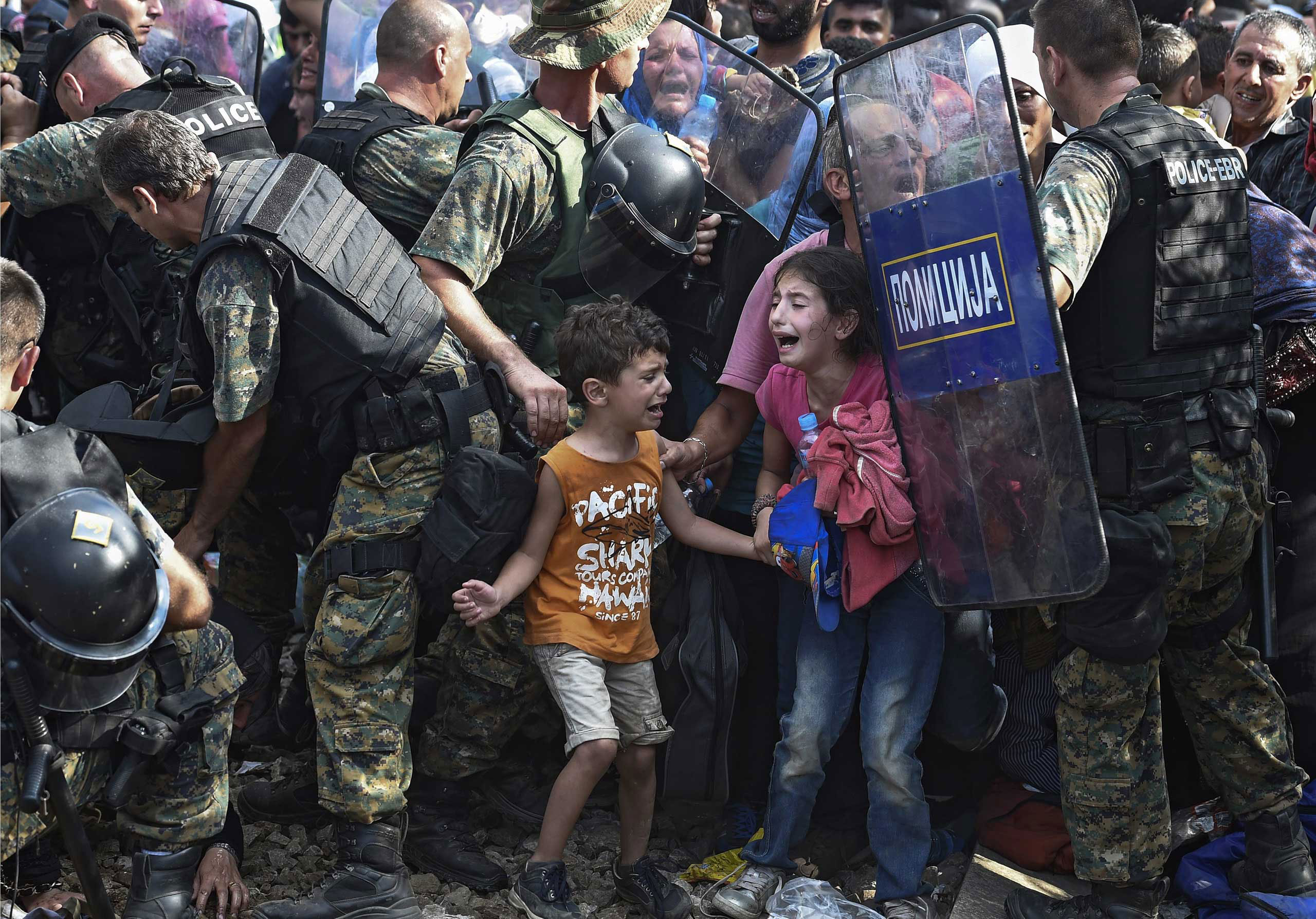 Children cry as migrants waiting on the Greek side of the border break through a cordon of Macedonian special police forces to cross into Macedonia, near the southern city of Gevgelija, The Former Yugoslav Republic of Macedonia. Aug. 21, 2015.