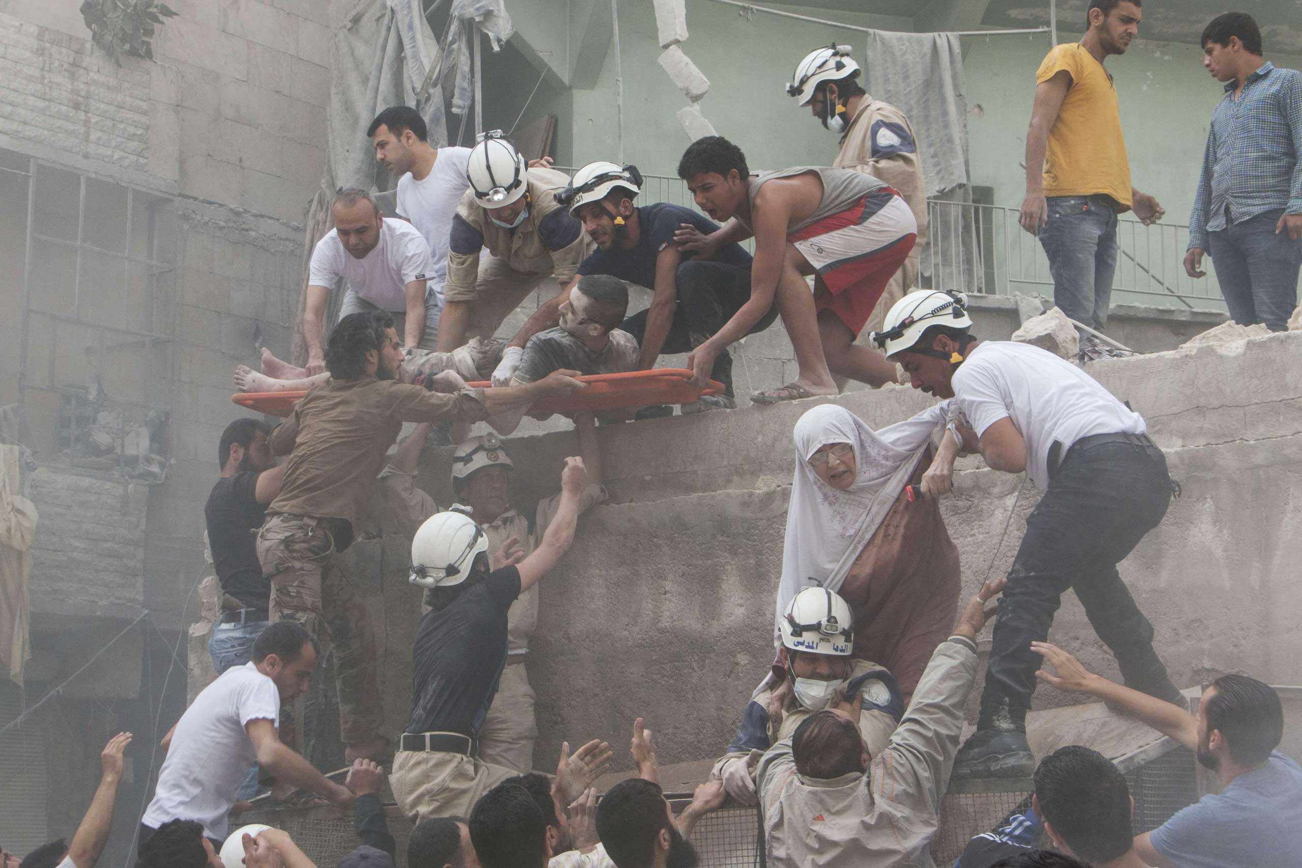 Syrian rescue workers and citizens evacuate people from a building following a reported barrel bomb attack by Syrian government forces on the central al-Fardous rebel-held neighborhood in the northern Syrian city of Aleppo. June 9, 2015.