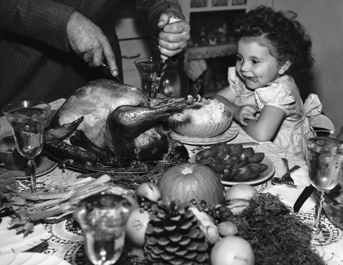 circa 1945:  A little girl sits at a table laden with dishes on Thanksgiving, watching anxiously as a man carves the turkey. (American Stock Archive / Getty Images)