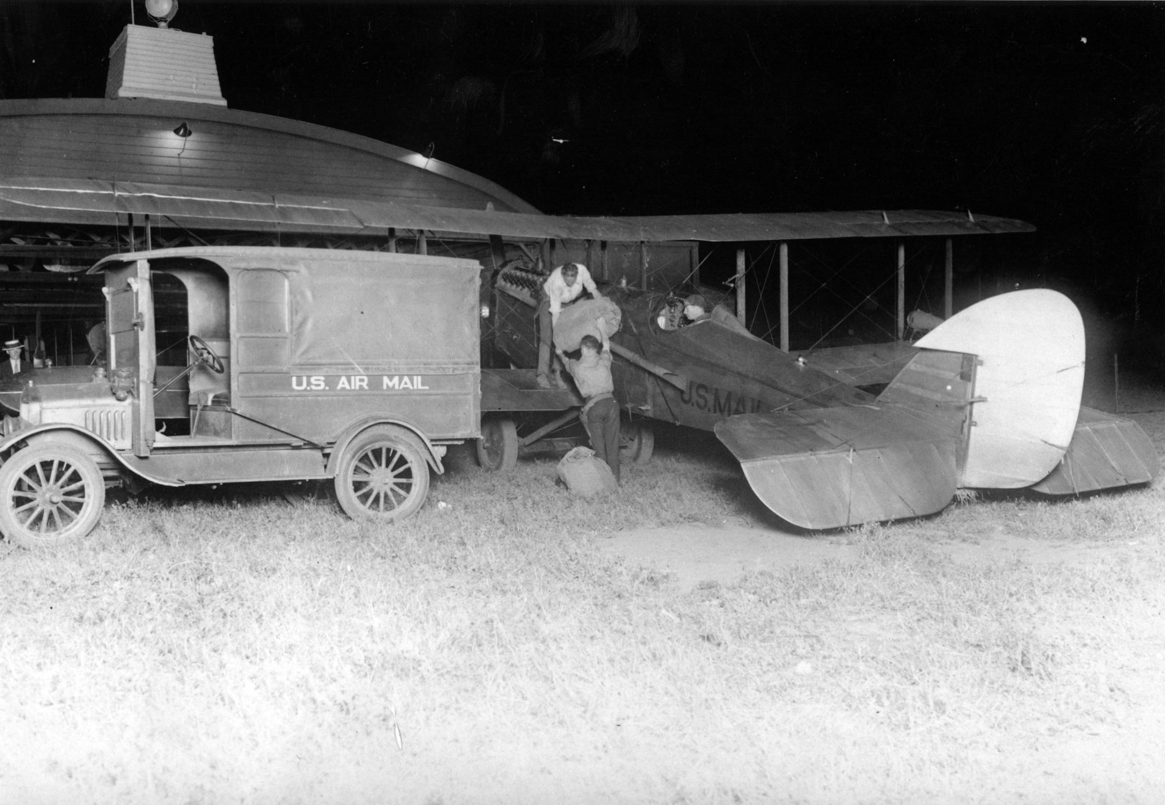 Postal employees loading mail into a de Havilland mail airplane at Hadley Field in New Brunswick, New Jersey. Regularly scheduled transcontinental airmail service, which had begun in the summer of 1924, was extended to east coast with the completion of a series of airmail beacons that helped guide pilots across the country. Airmail pilots Dean Smith and James DeWitt Hill carried mail out of Hadley Field on the of July 1, 1925. Smith ran out of gas and crashed outside of Cleveland, Ohio. Hill reached Cleveland with his mail, which was transferred onto airplanes with new pilots for the next part of the transcontinental journey.