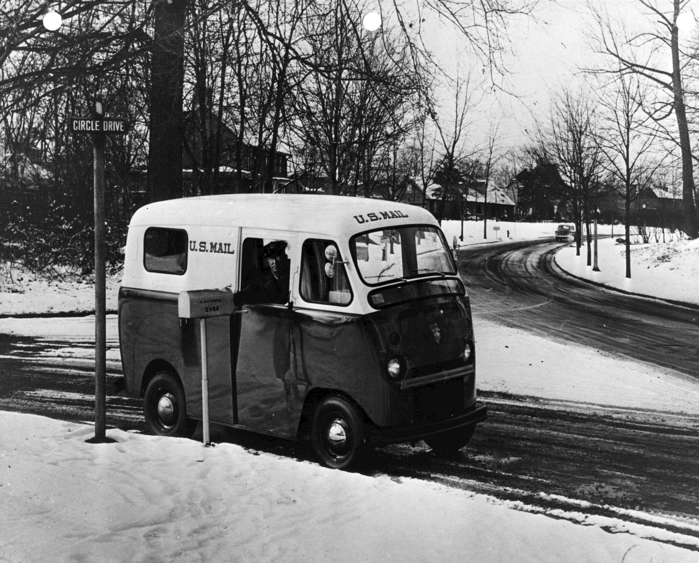 A letter carrier drives one of the Department’s new right-hand drive vans on the snowy streets of an unidentified city. The Department ordered thousands of new postal vehicles in the early 1950s as part of its post-war modernization plan. A variety of vehicles were ordered, including right-hand drive step vans such as this. Many of the new vehicles performed adequately, but few of the dozens of different styles ordered were re-ordered in large quantities. 1953.