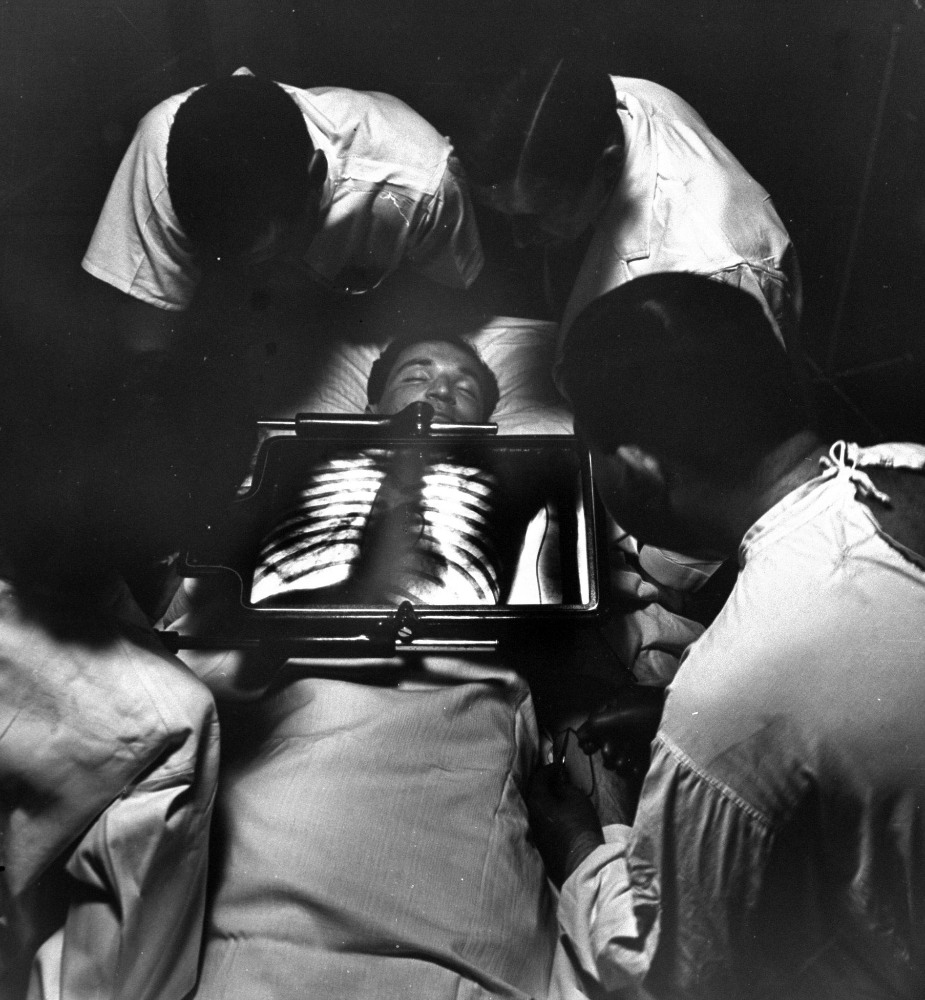 Doctors using x-ray machine to feed venous catherter into patient's heart, 1947.