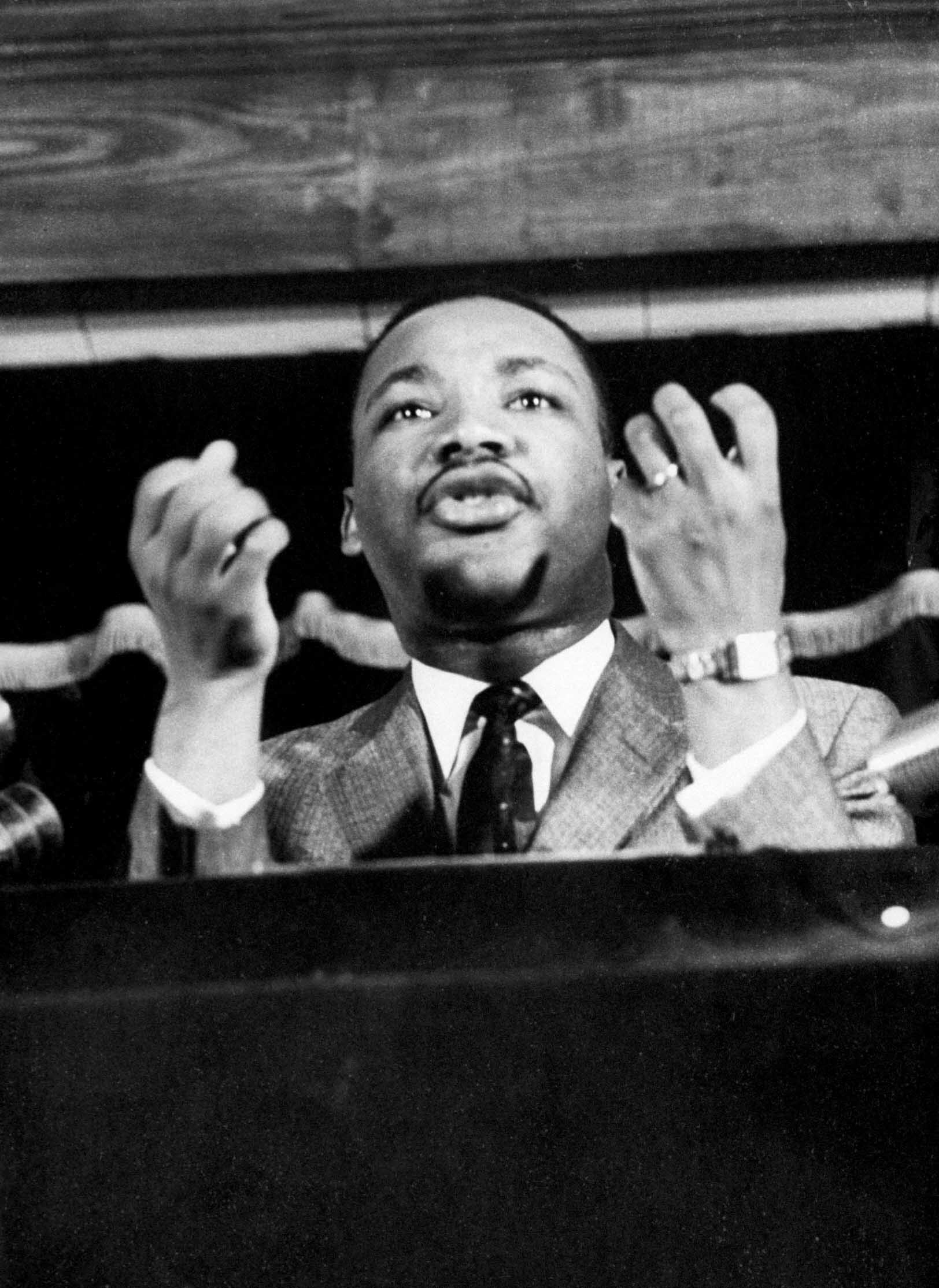 Civil rights leader Rev. Martin Luther King speaking from pulpit at mass meeting about principles of non-violence before leading assembly to ride newly integrated busses after successful boycott.
