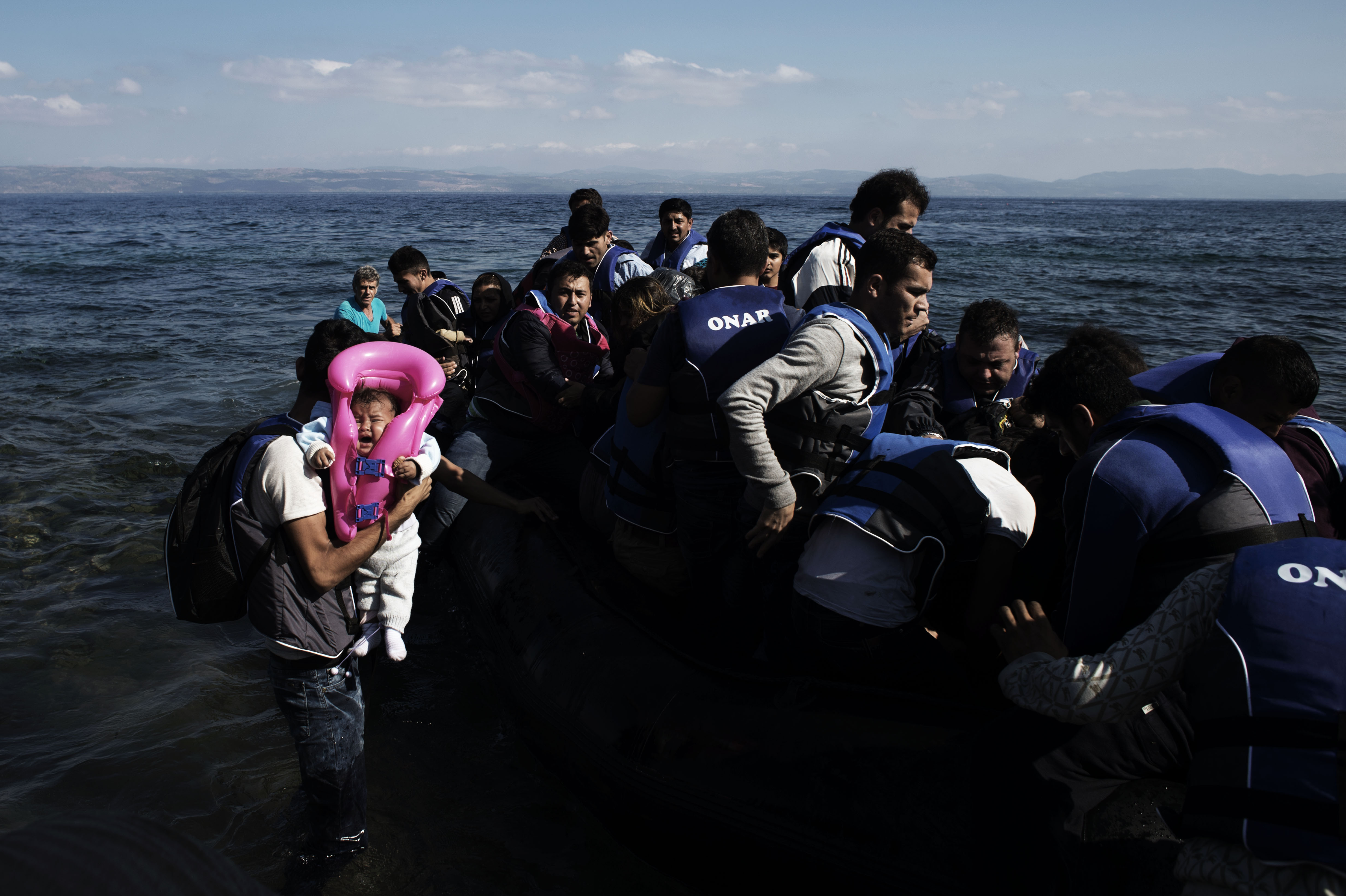 Asylum-seekers from the Syrian Arab Republic, including a crying infant, begin to disembark a large raft as they arrive on the shores of the island of Lesbos, in the North Aegean region on Sept. 14, 2015.