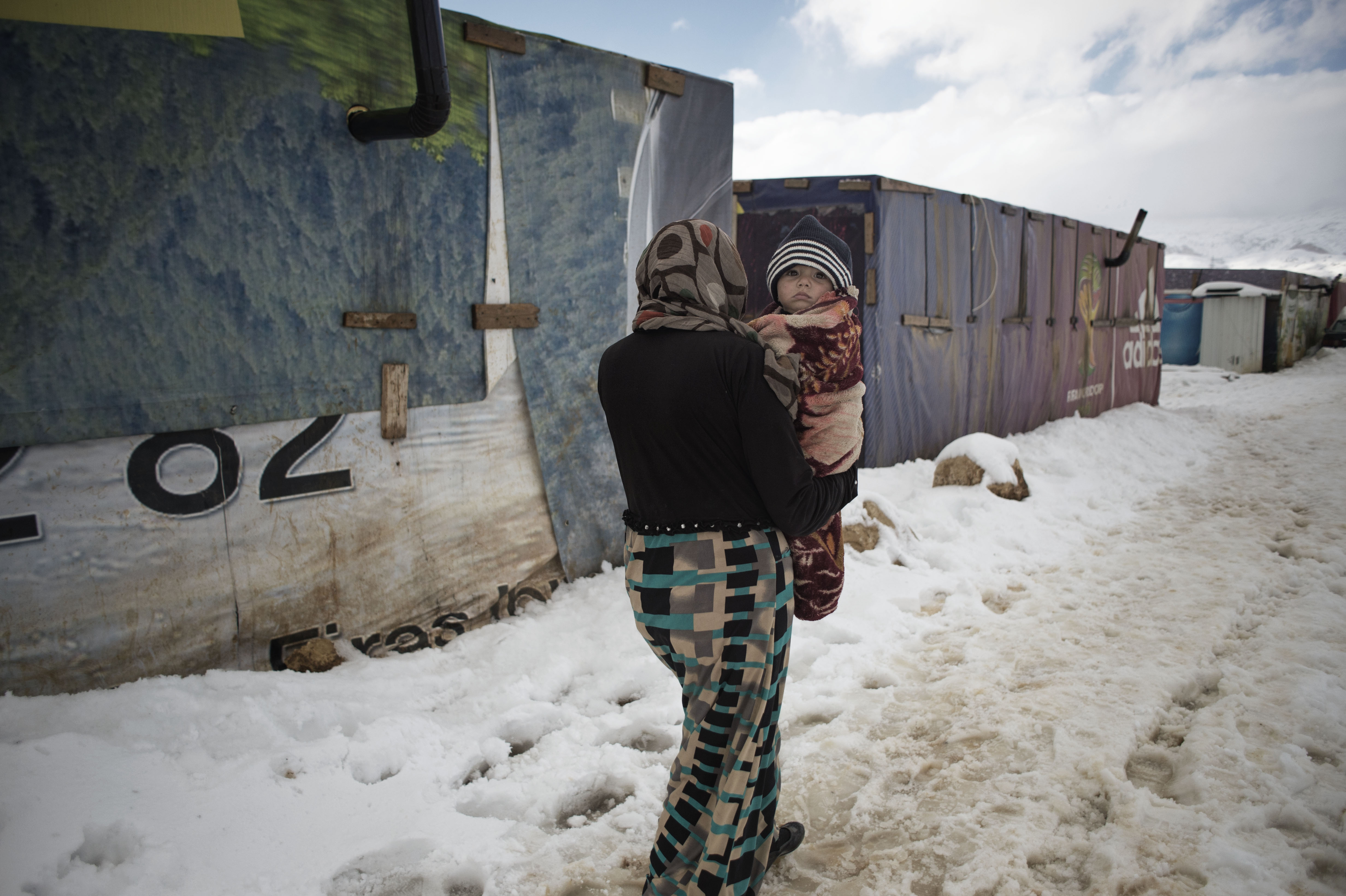 Walking through snow, a woman carries an infant in refugee camp number 29, in the Bekaa Valley of Lebanon on Jan. 8, 2015.