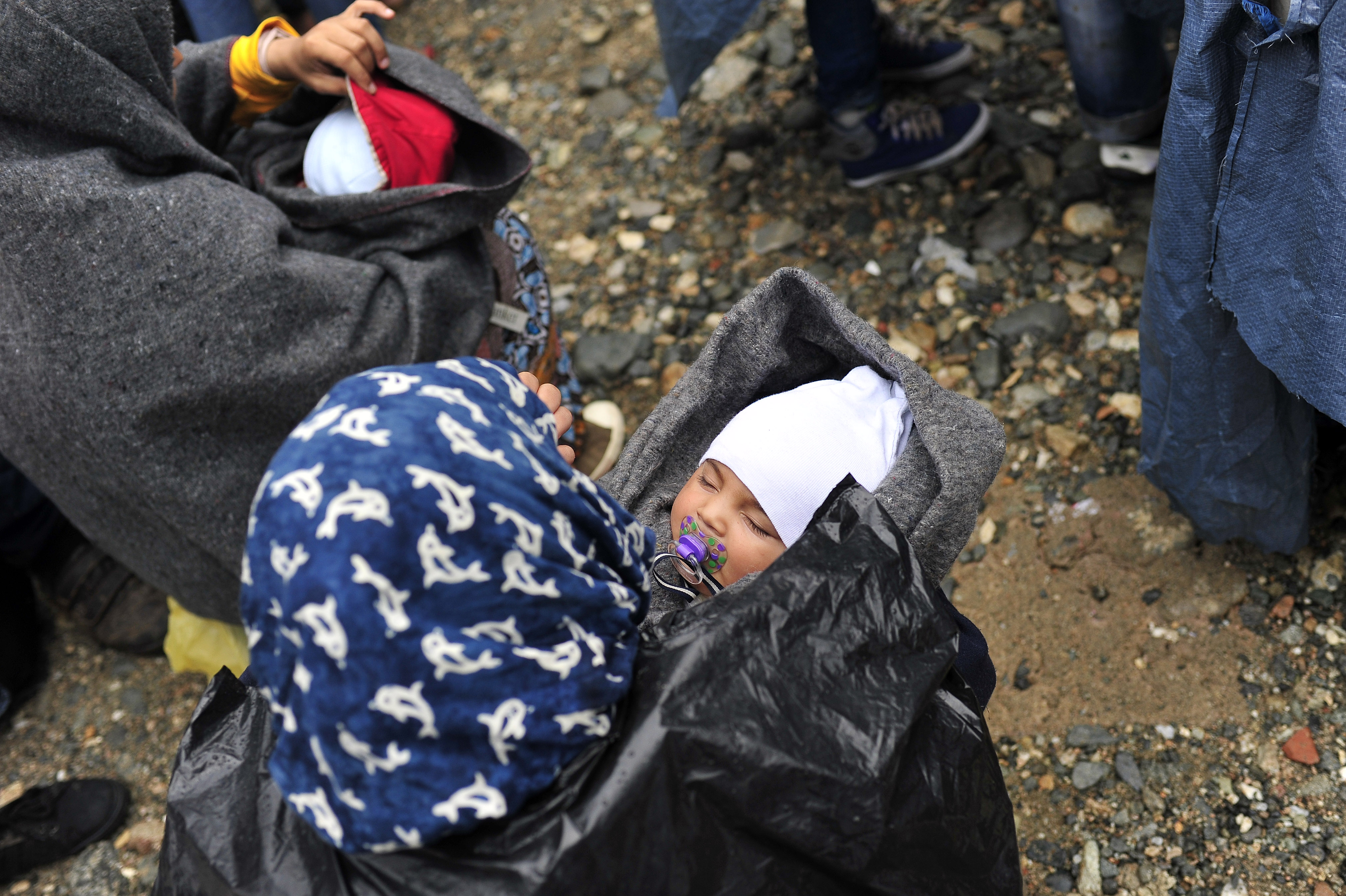 Seated on the wet, rocky ground, a woman holds an infant on a rainy day, near the town of Gevgelija, on the border with Greece on Sept. 10, 2015. Others who have fled their homes amid the ongoing refugee and migrant crisis are nearby.