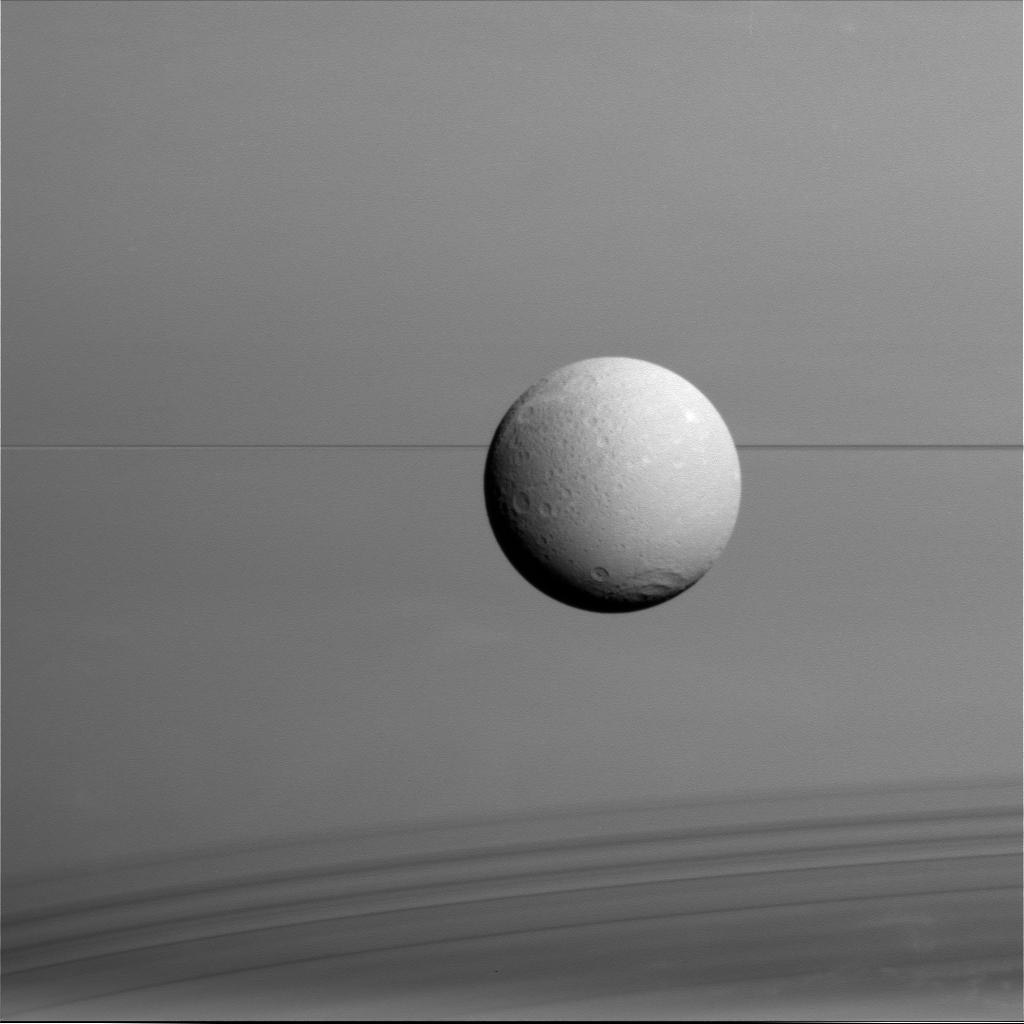 The Saturnian moon Dione hangs in front of Saturn and its icy rings in this view, captured during the Cassini spacecraft's final close flyby of the icy moon on Aug. 17, 2015.