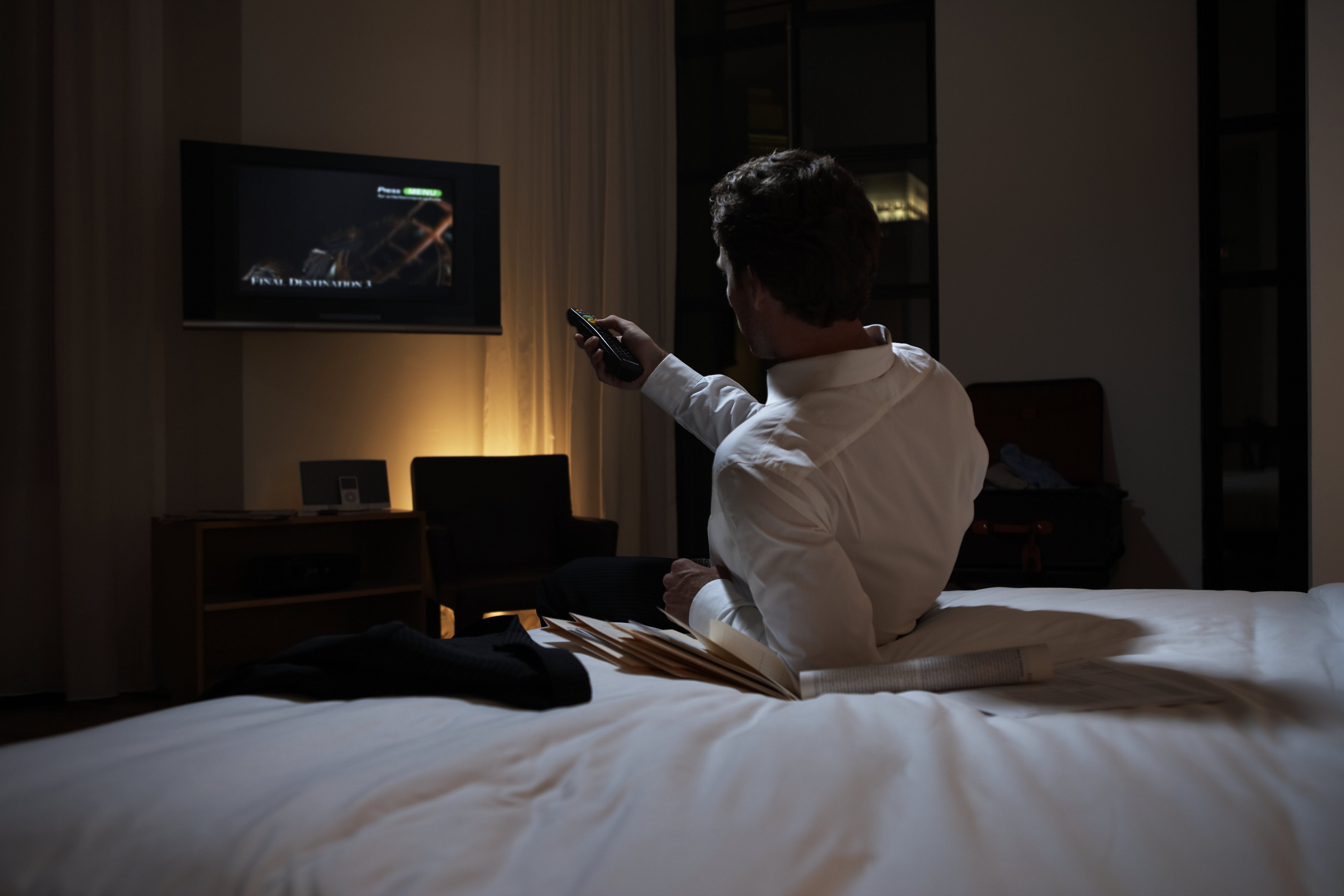 Man on hotel bed watching TV. (Leonard McLane&mdash;Getty Images)