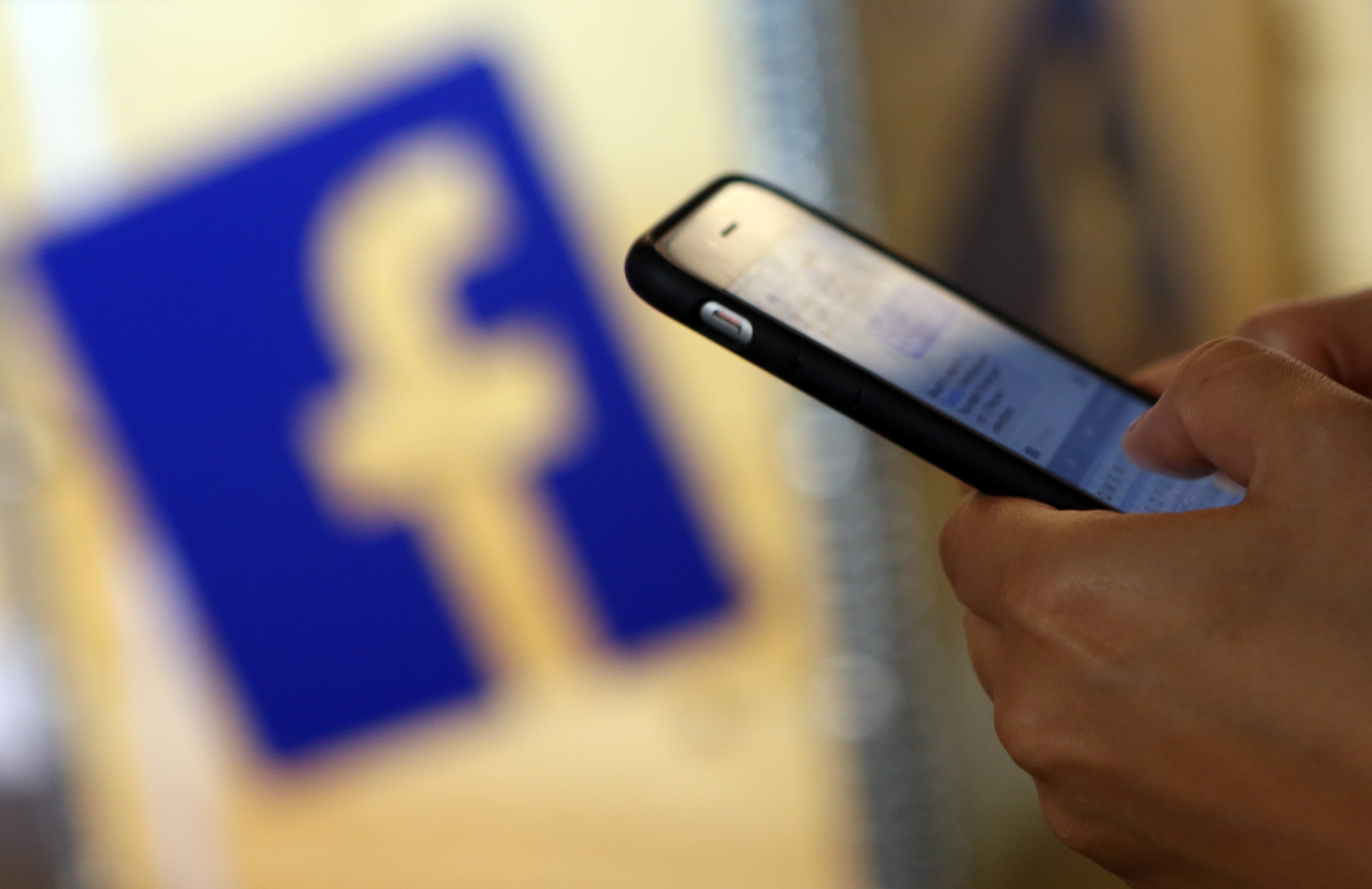 A visitor uses a mobile phone in front of the Facebook logo on Sept. 12, 2015. (Adam Berry—Getty Images)