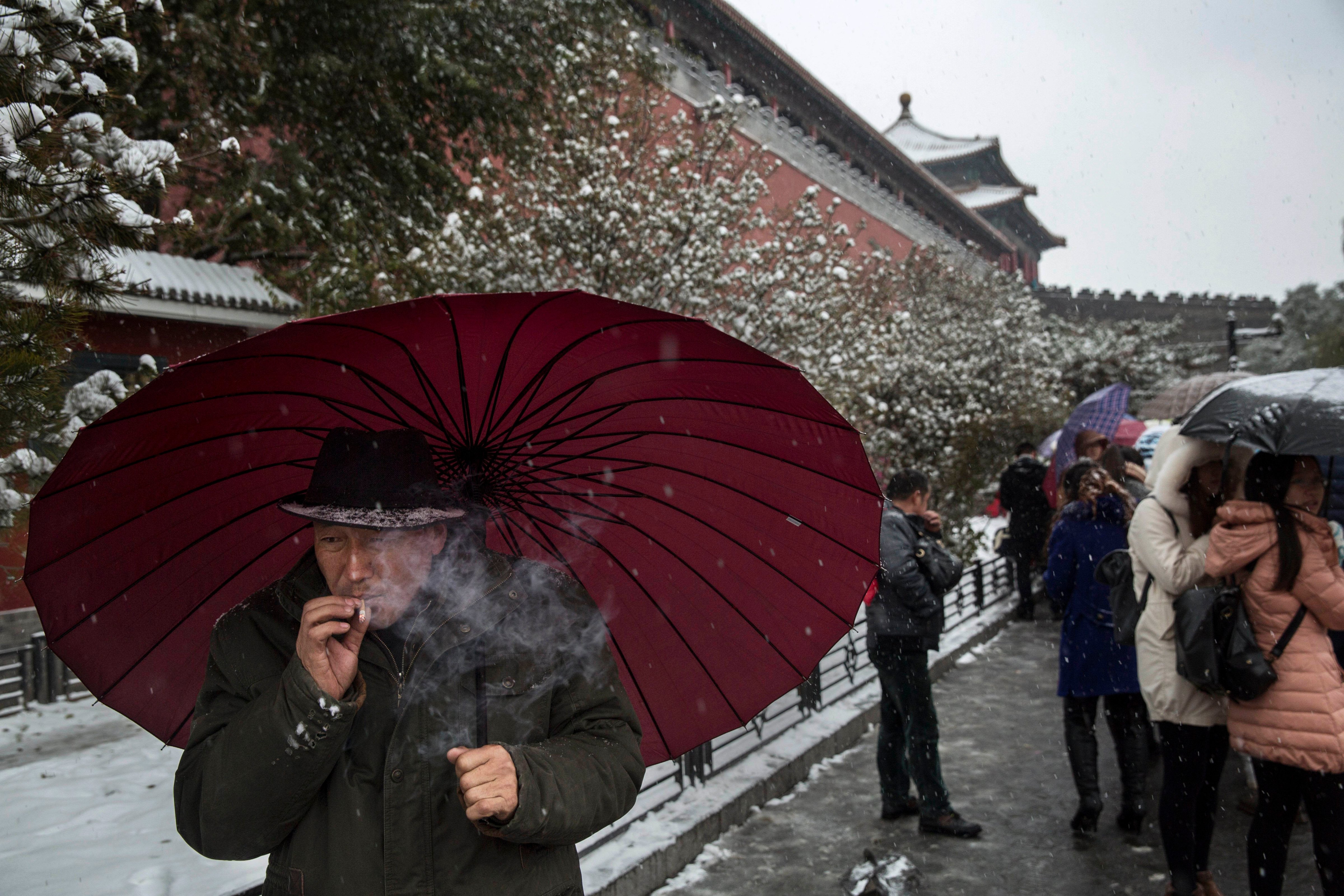 A Chinese man smokes as he shields himself under an umbrella from the snow during a snowfall on November 22, 2014 outside the Forbidden City in Beijing, China. (Kevin Frayer—Getty Images)