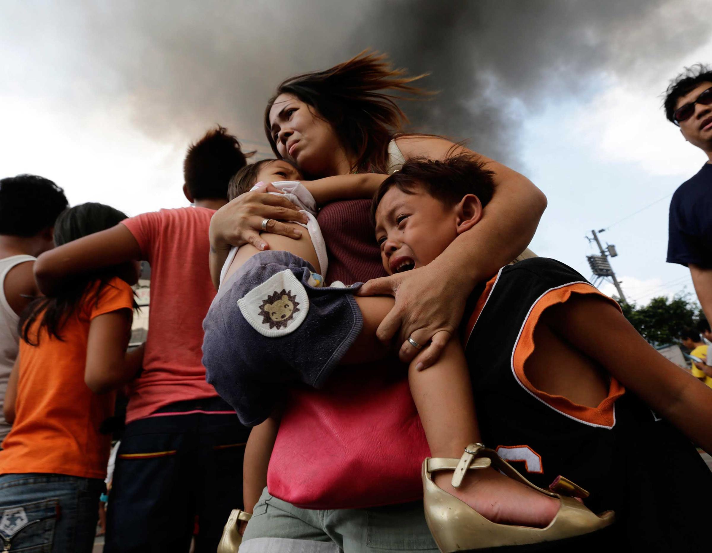 A Filipino mother carries her children while their house is on fire in a residential slum area in Manila, Philippines, April 29, 2014. The Manila Fire Department said that the fire left more than thirty families homeless and three residents were hurt.