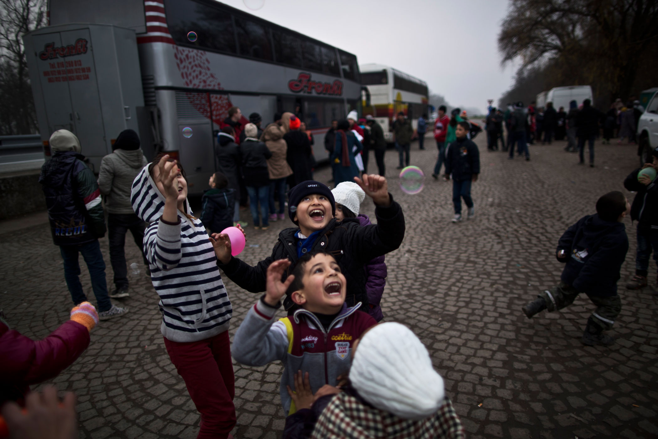 Dildar Qasu, 10, chases bubbles with other children in Adasevci, Serbia, while waiting to be transported via bus to Sid, where authorities load trains headed to Croatia, Dec. 6, 2016.