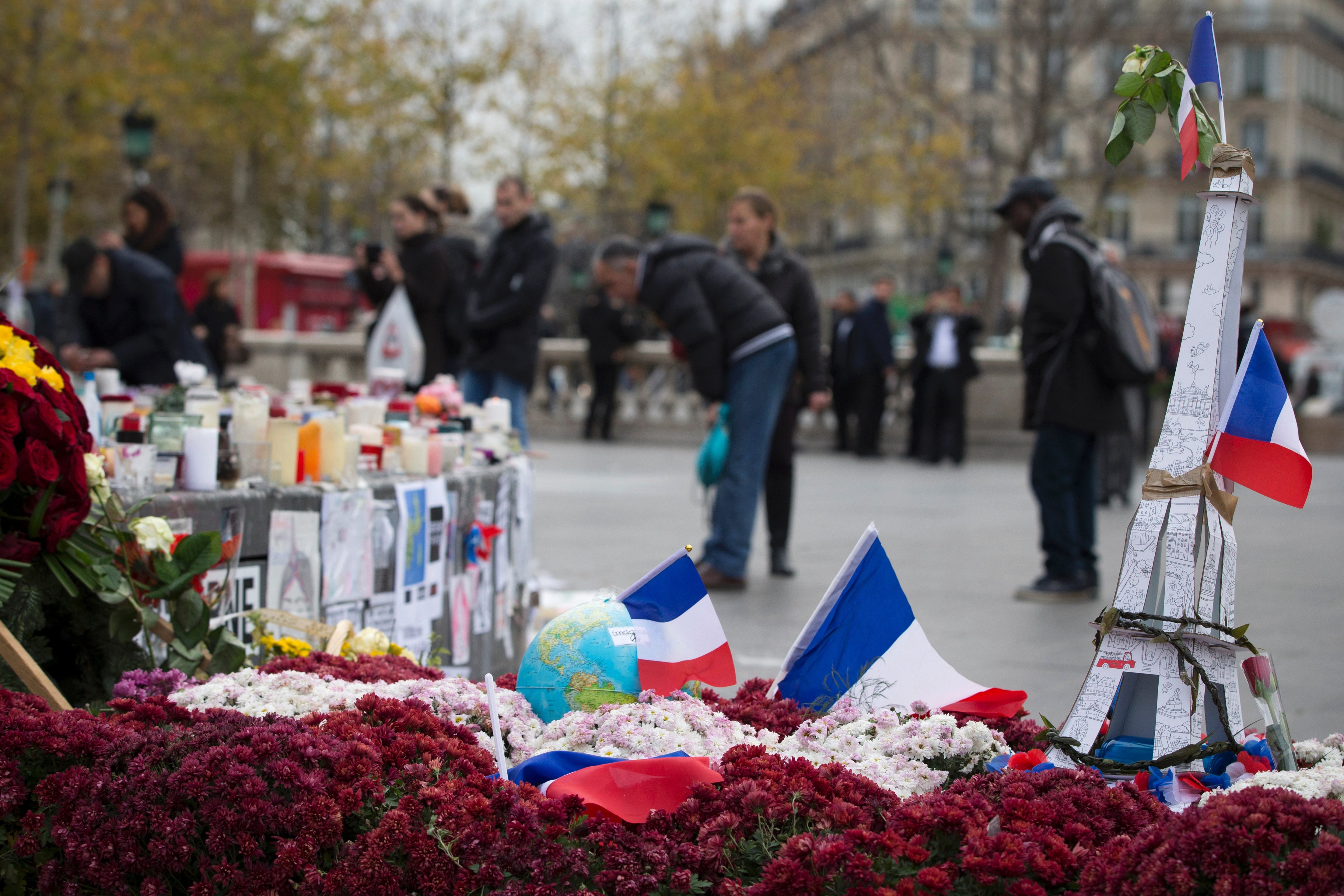 People stand on the Place de la Republique in Paris on December 2, 2015, next to a model Eiffel Tower, flowers and French flags layed in memory of the victims of the deadly attacks in and around Paris on Nov. 13.