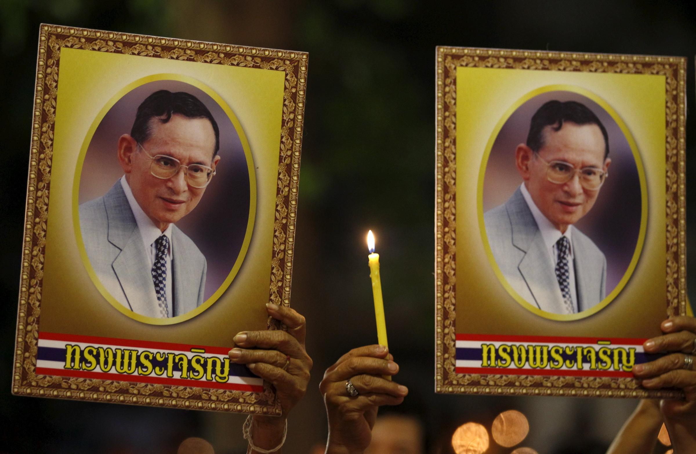 Well-wishers hold a lit candle and portraits of Thailand's King Bhumibol Adulyadej at Siriraj hospital, where a group has gathered to mark his 88th birthday, in Bangkok