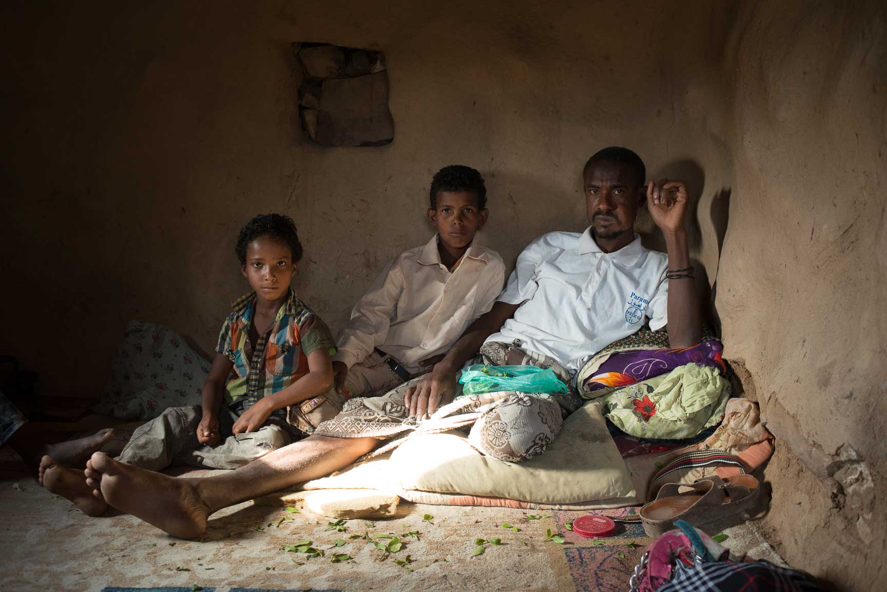 Fadhl Ahmad, a guard for the qat fields, sits with his two sons in his home on July 22, 2015. Since the war started, there has been no diesel to pump the water to water the qat, so he’s had no work.