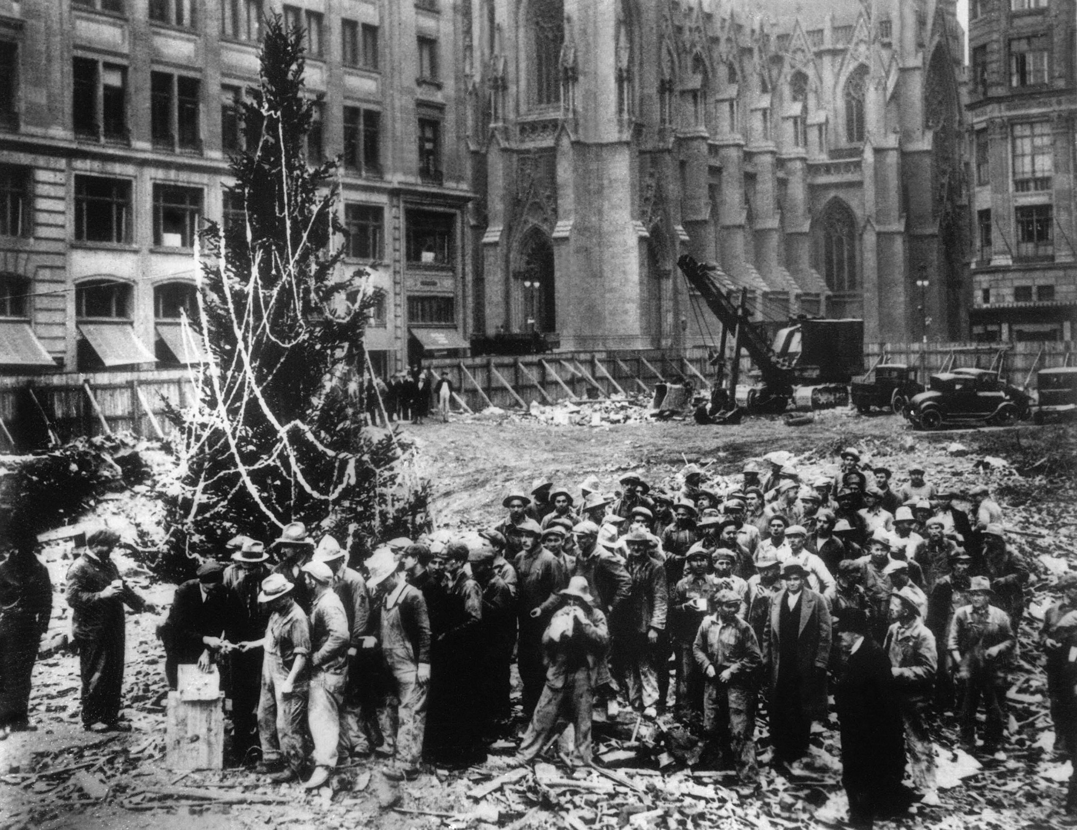 Construction workers line up for pay beside the first Rockefeller Center Christmas tree in New York, 1931. The Christmas tree went on to become an annual tradition and a New York landmark. St. Patrick's Cathedral is visible in the background on Fifth Avenue.