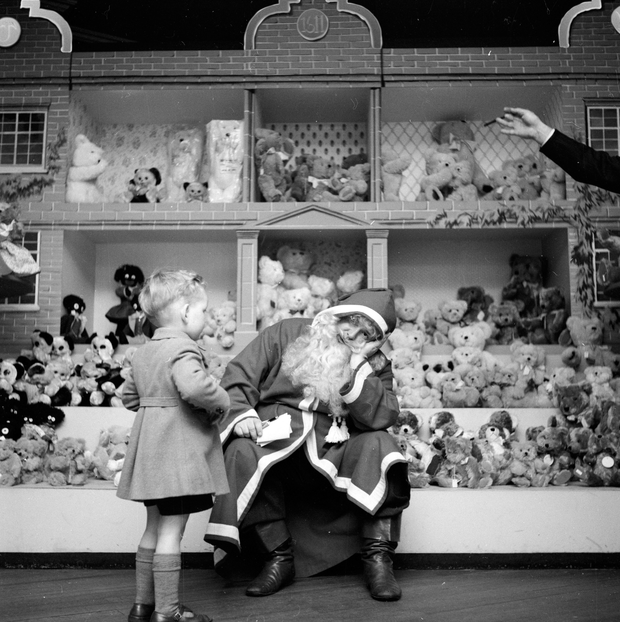 A resolutely tired Denzil Batchelor, in costume as Father Christmas, wearily answers another child's question at Harrods department store in London. December 1953.