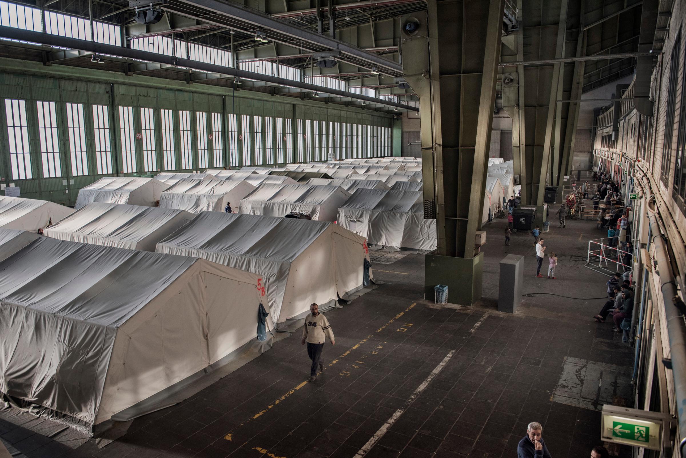 Cabins and tents are set up inside hangers of the former Berlin Tempelhof Airport, now to be used as temporary shelter for migrants, refugees and asylum seekers in Berlin. Germany, Dec. 2015. Used by the Nazis and once one of the world's largest buildings, today the Berlin Tempelhof Airport is being used as a major shelter for refugees and asylum seekers as Germany struggles to house the biggest influx of migrants since World War II.