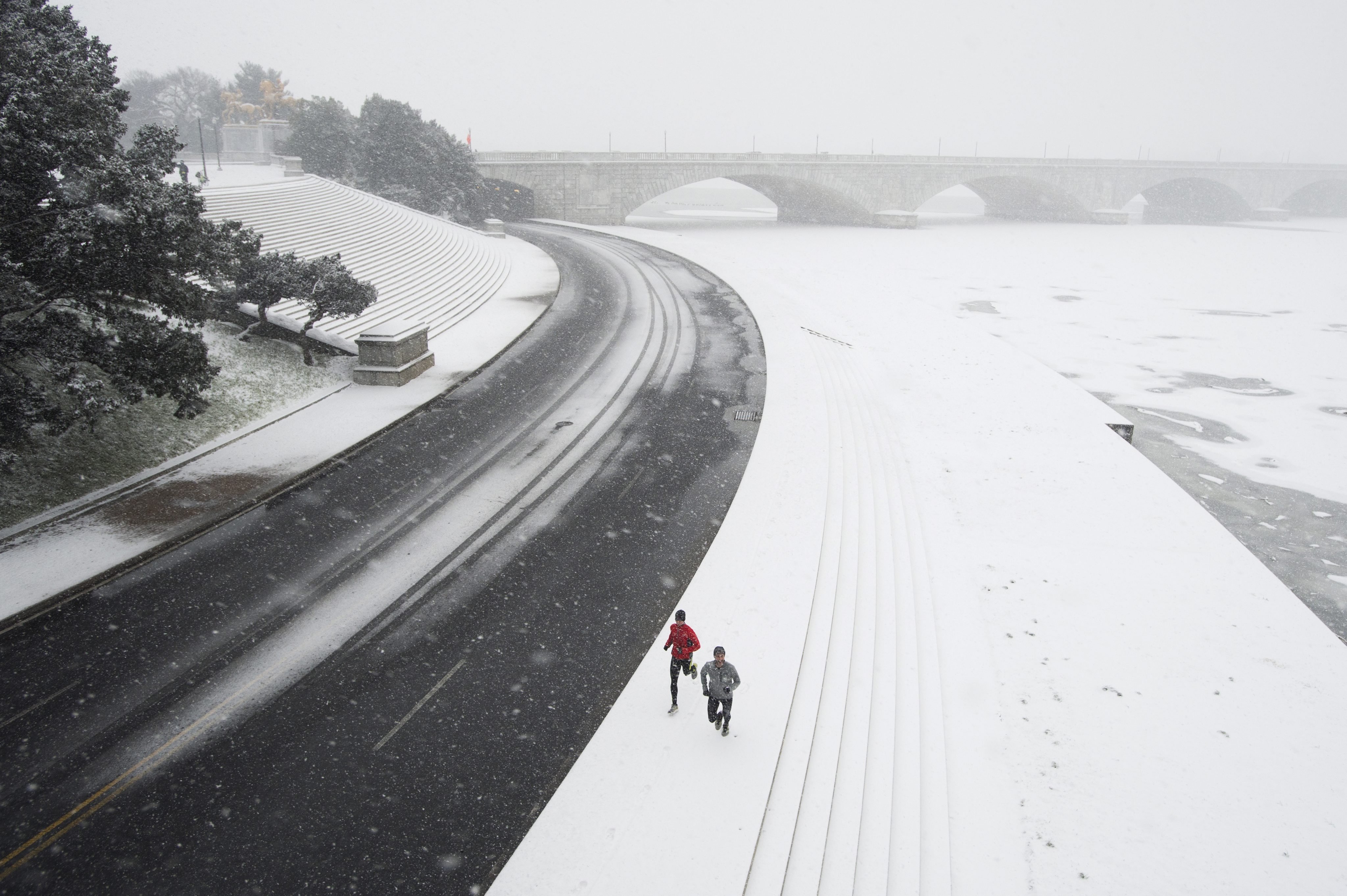 Joggers run by the Potomac River with the Memorial Bridge seen behind, during a snowstorm in Washington, DC on Jan. 22, 2016.