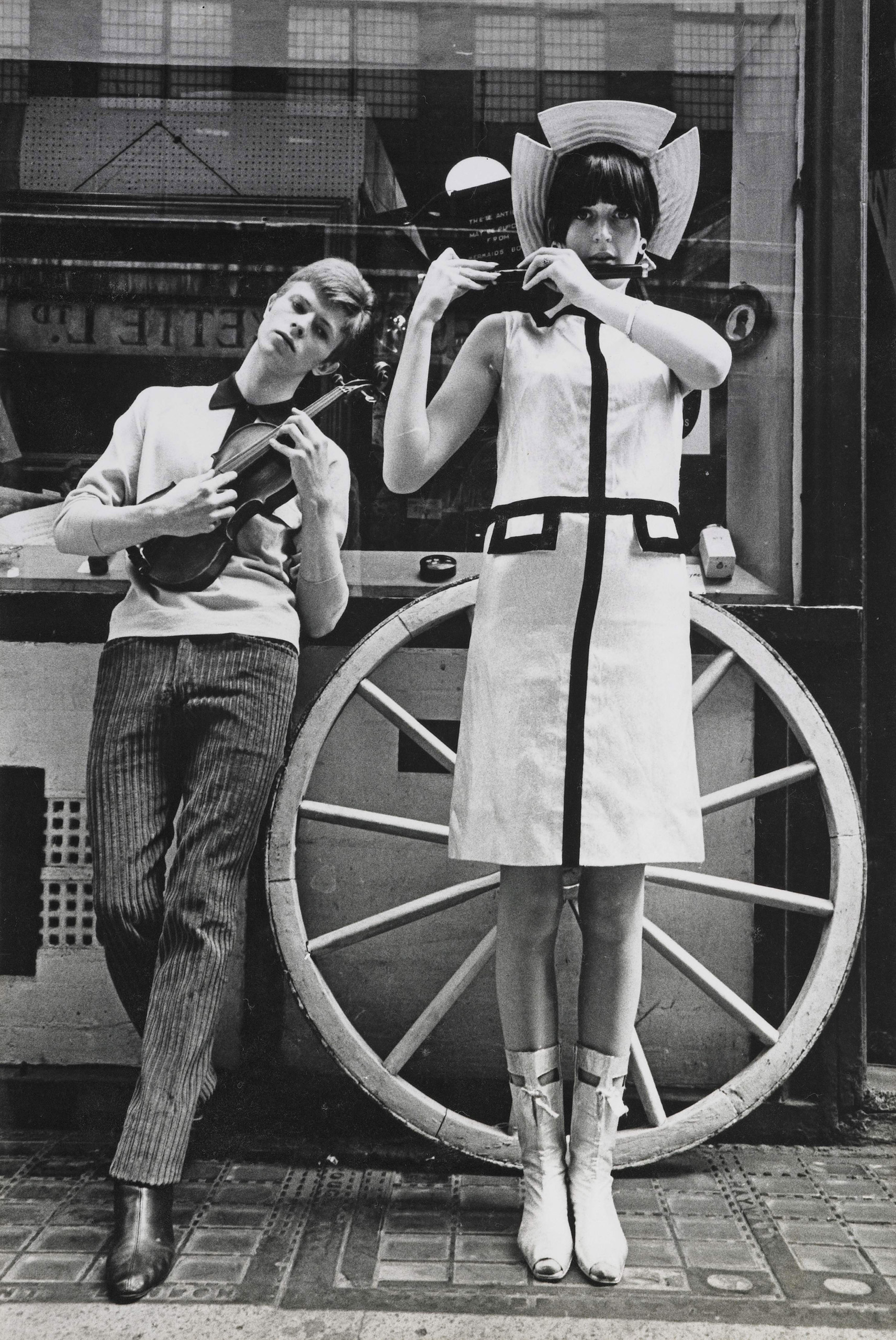 David Bowie playing mandolin with a model. Photo taken on Kingly Street, off Carnaby Street in the summer of 1963, UK.