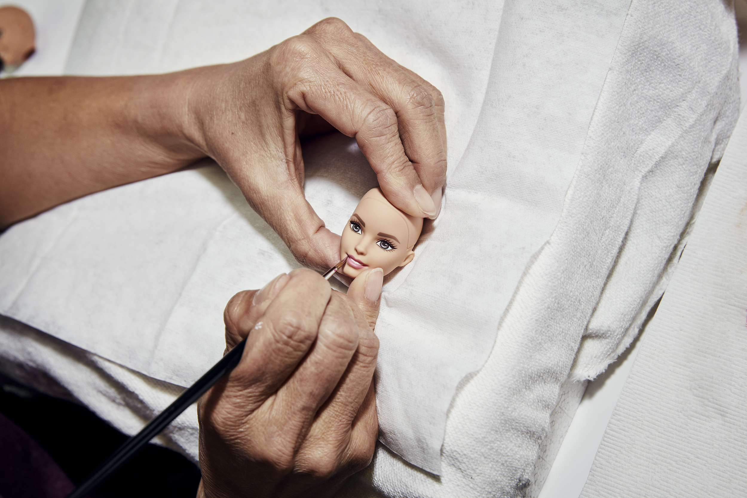 A designer hand paints the lips of a prototype Barbie doll.