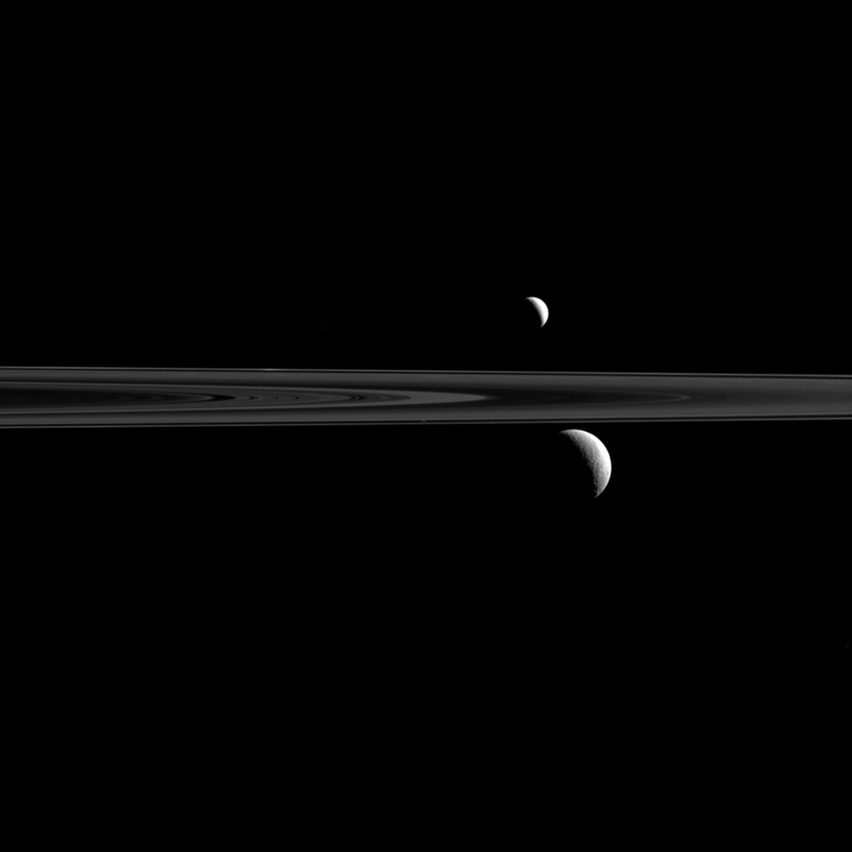The Cassini spacecraft captures Enceladus above Saturn's rings and Rhea below. The tiny speck of Atlas can also be seen just above and to the left of Rhea, and just above the thin line of Saturn's F ring. The image was taken in visible light with the Cassini spacecraft narrow-angle camera on Sept. 24, 2015.