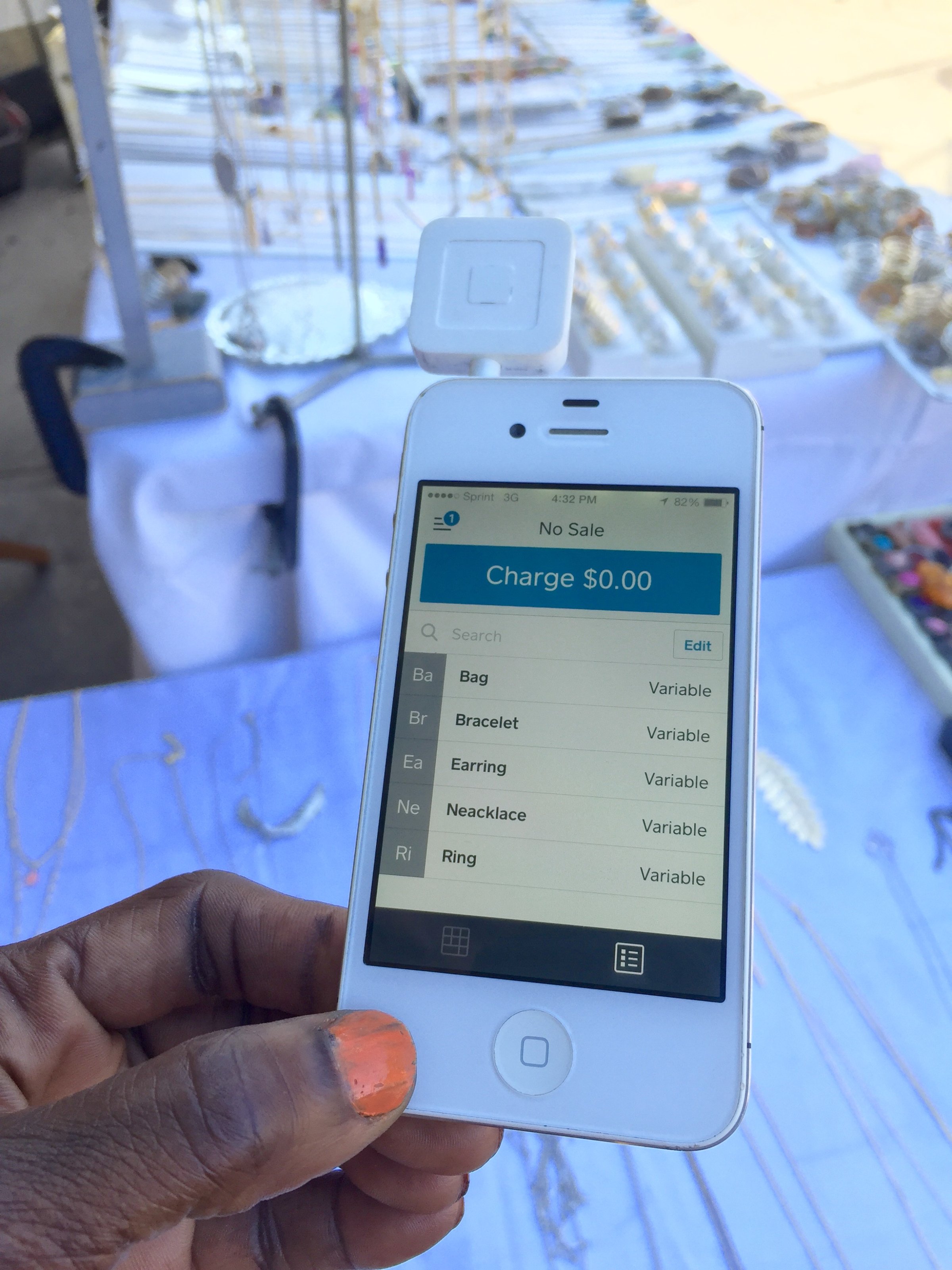 Technology Helps: A jewelry vendor at an outdoors craft market holds her credit card reader attached to a smart device for mobile point of sales activity