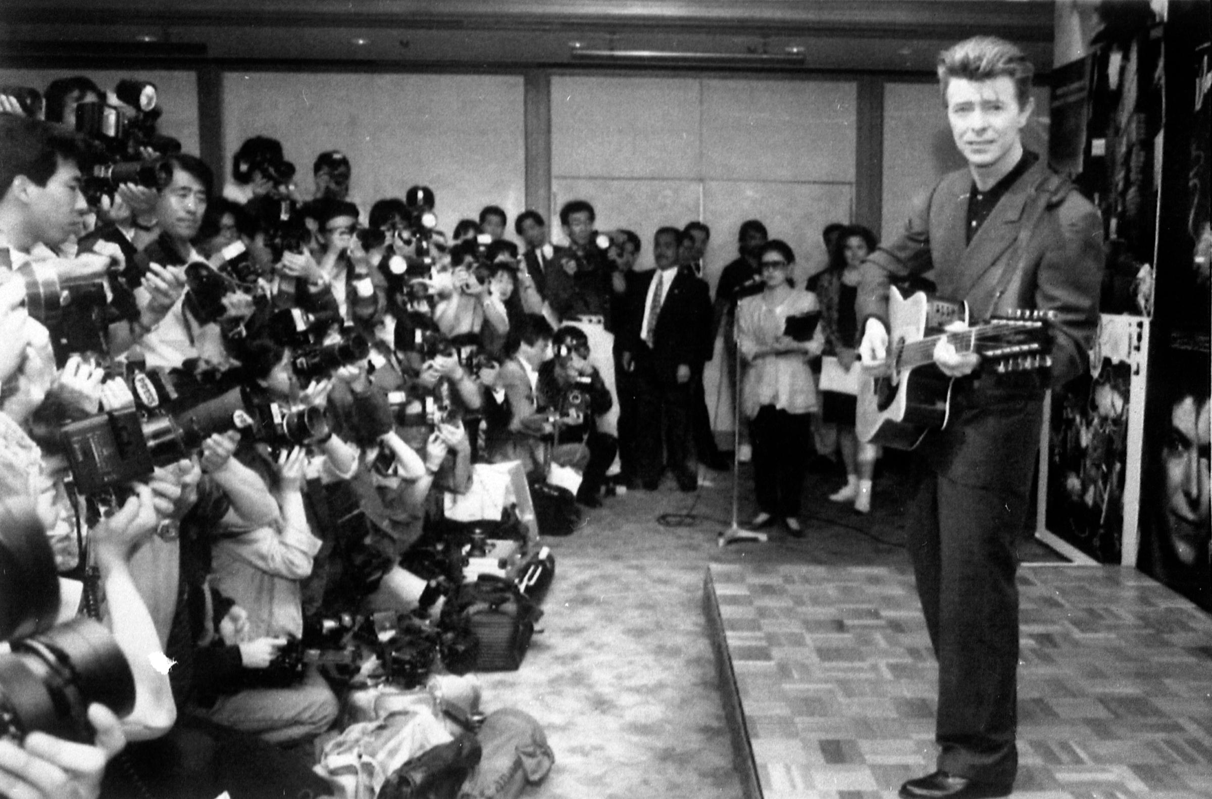 David Bowie plays an acoustic guitar while being photographed at a press conference in Tokyo on May 19, 1990.