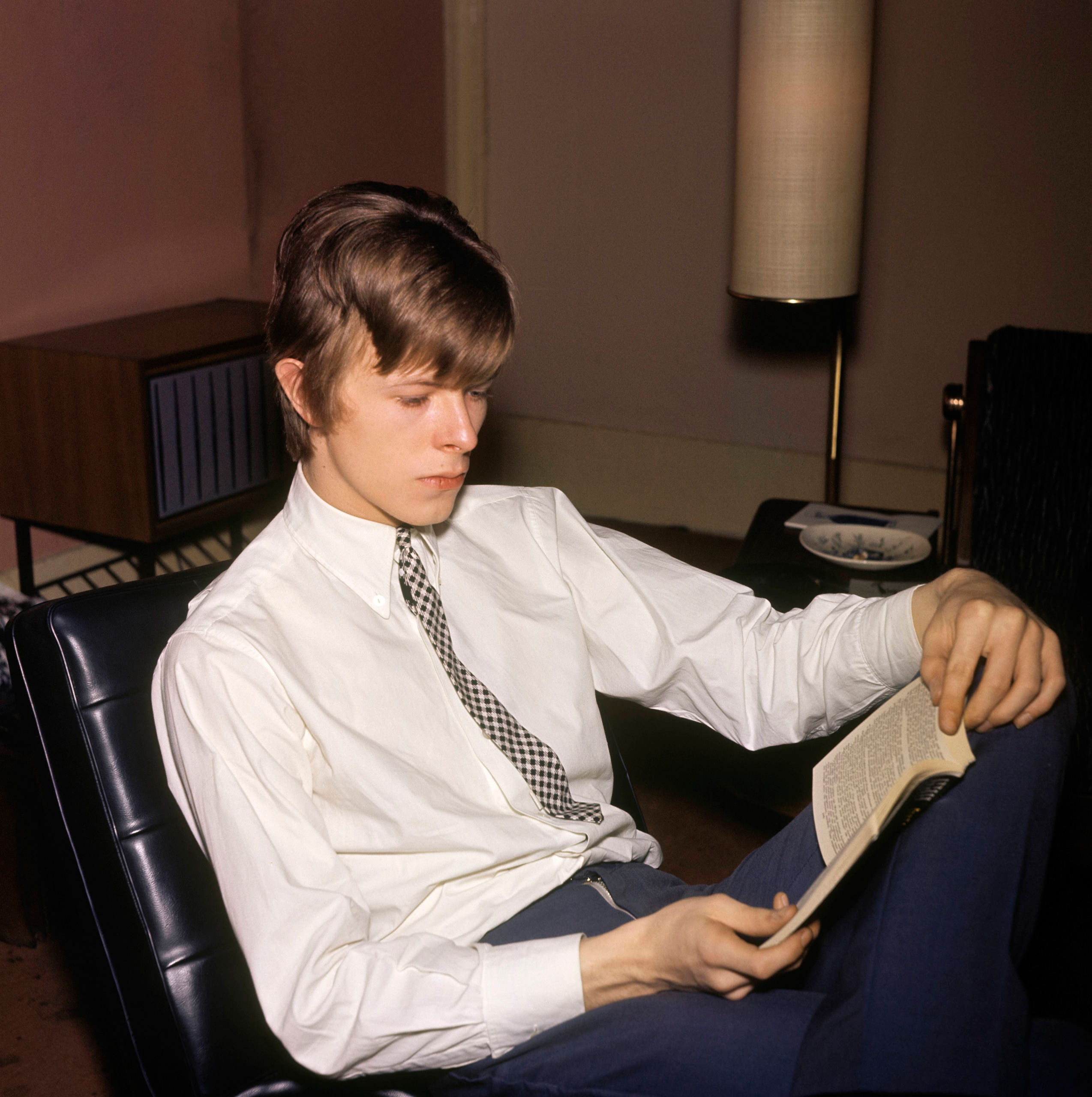 David Bowie photographed reading a book, c. 1965. (CA/Redferns)