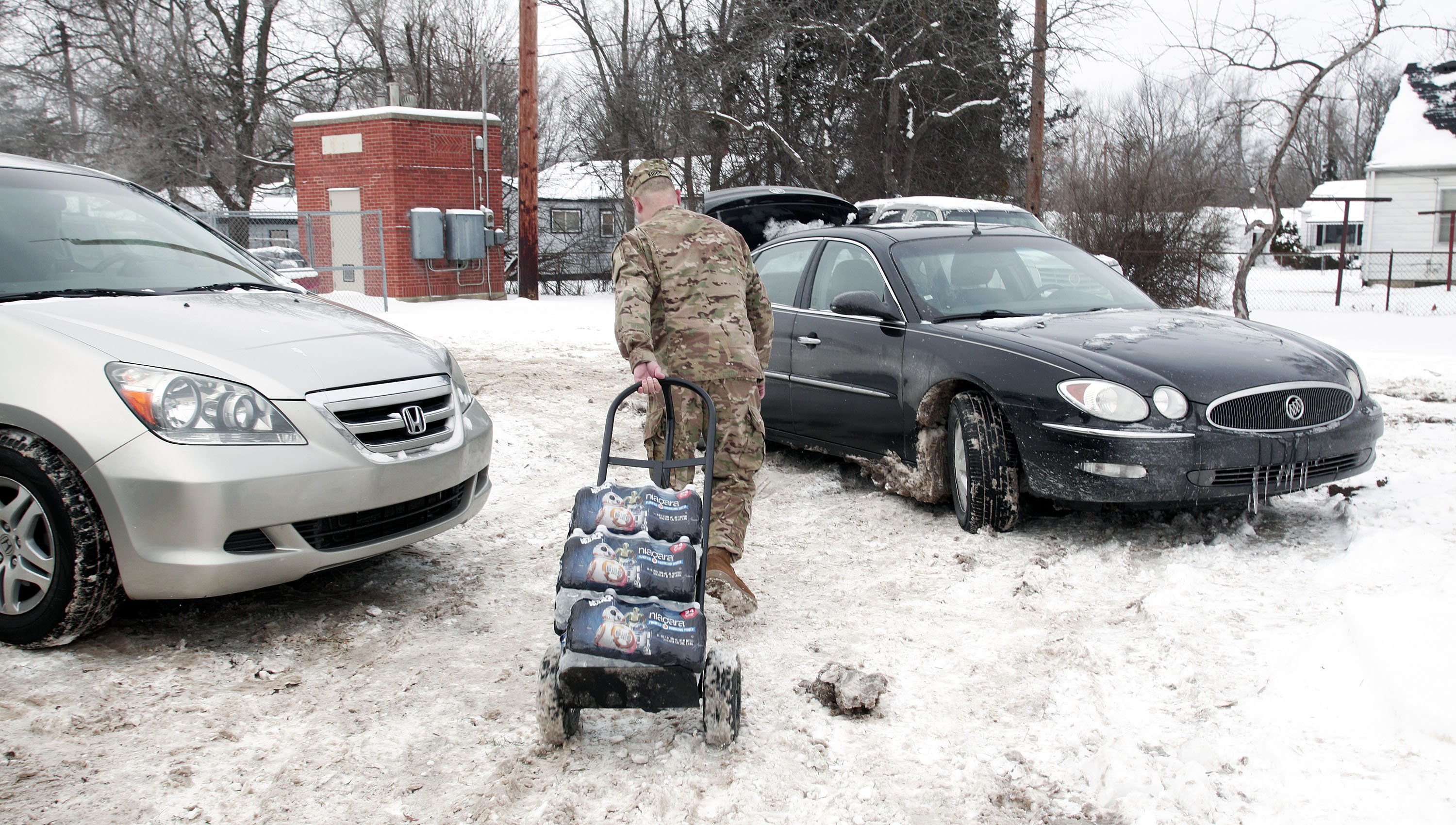 Michigan National Guard Staff Sergeant Steve Kiger of Beaverton, Michigan, helps Christine Brown of Flint, Michigan take bottled water out to her car after she received it at a Flint Fire Station on Jan 13, 2016 in Flint, Michigan.