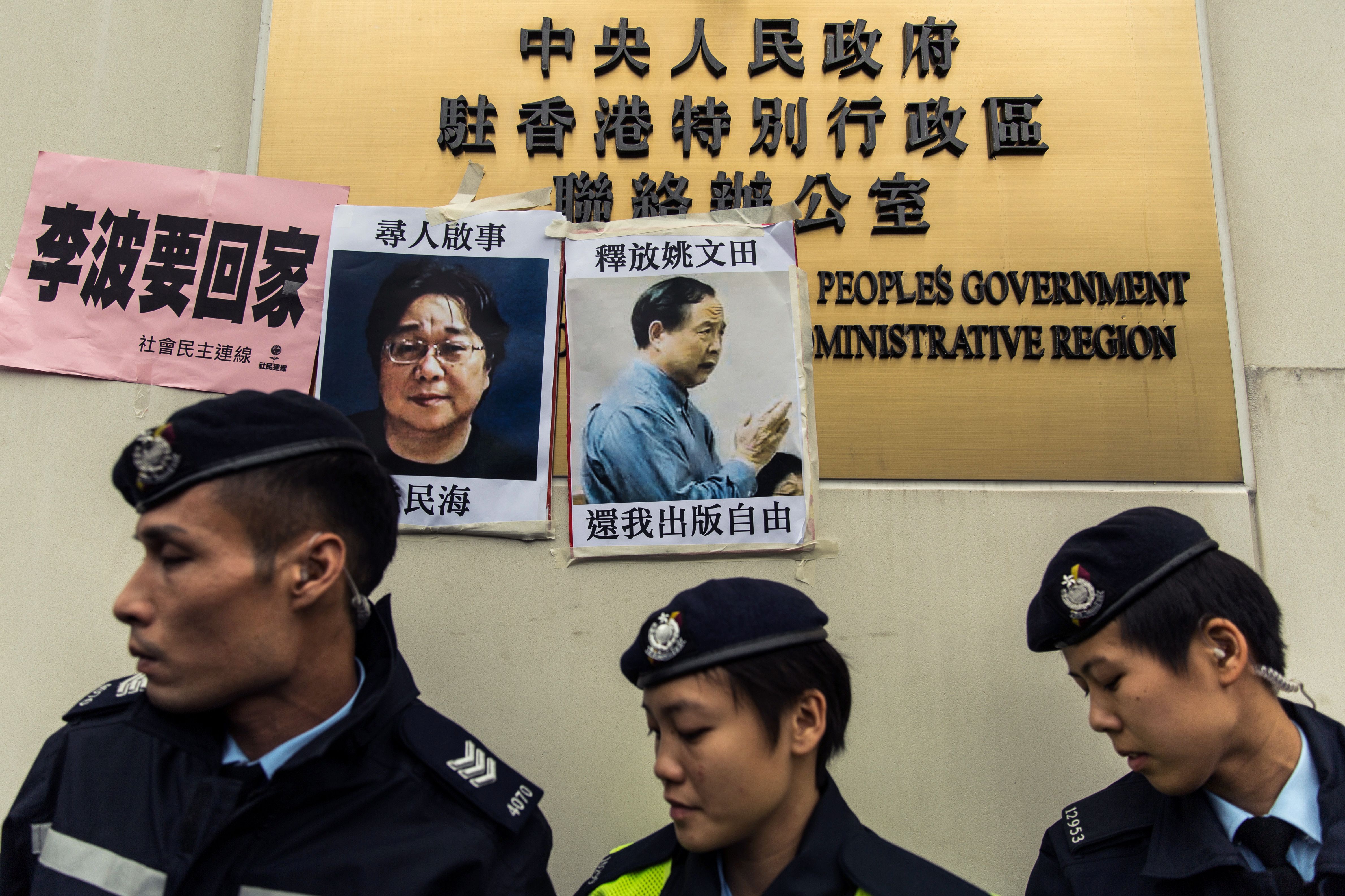 Police walk past missing-person notices for Gui Minhai, left, among five missing booksellers from the Mighty Current publishing house, and Yau Wentian, a Hong Kong publisher who was jailed for 10 years in 2015 while preparing to release a book critical of Chinese President Xi Jinping, posted on top of the sign of China's Liaison Office in Hong Kong on Jan. 3, 2016. (Anthony Wallace—AFP/Getty Images)