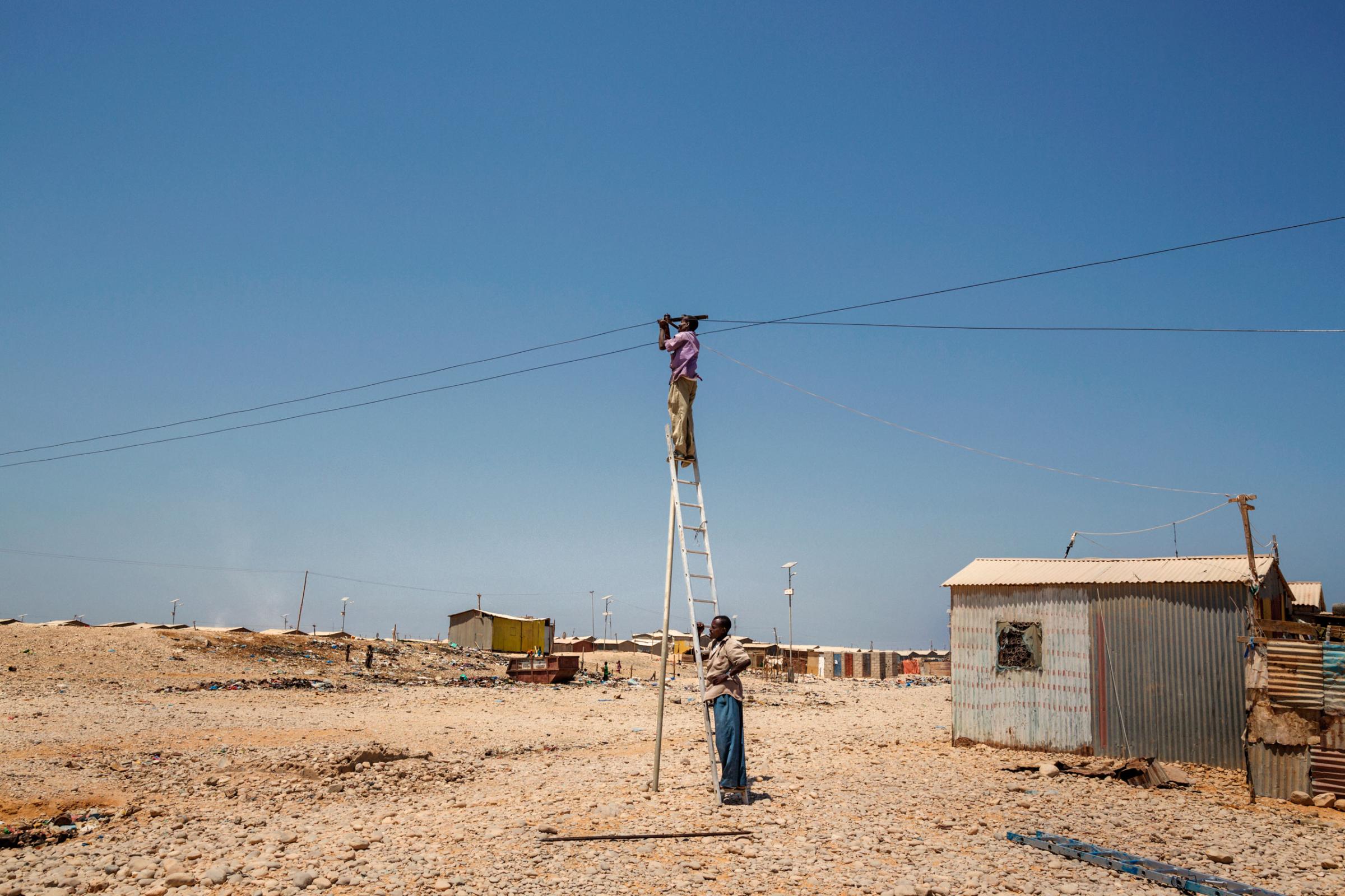 Two men working on a light pole in the Buulo Mingis camp for internally displaced people located in Bosaso, in the north-east zone of Somalia. October 5, 2015.