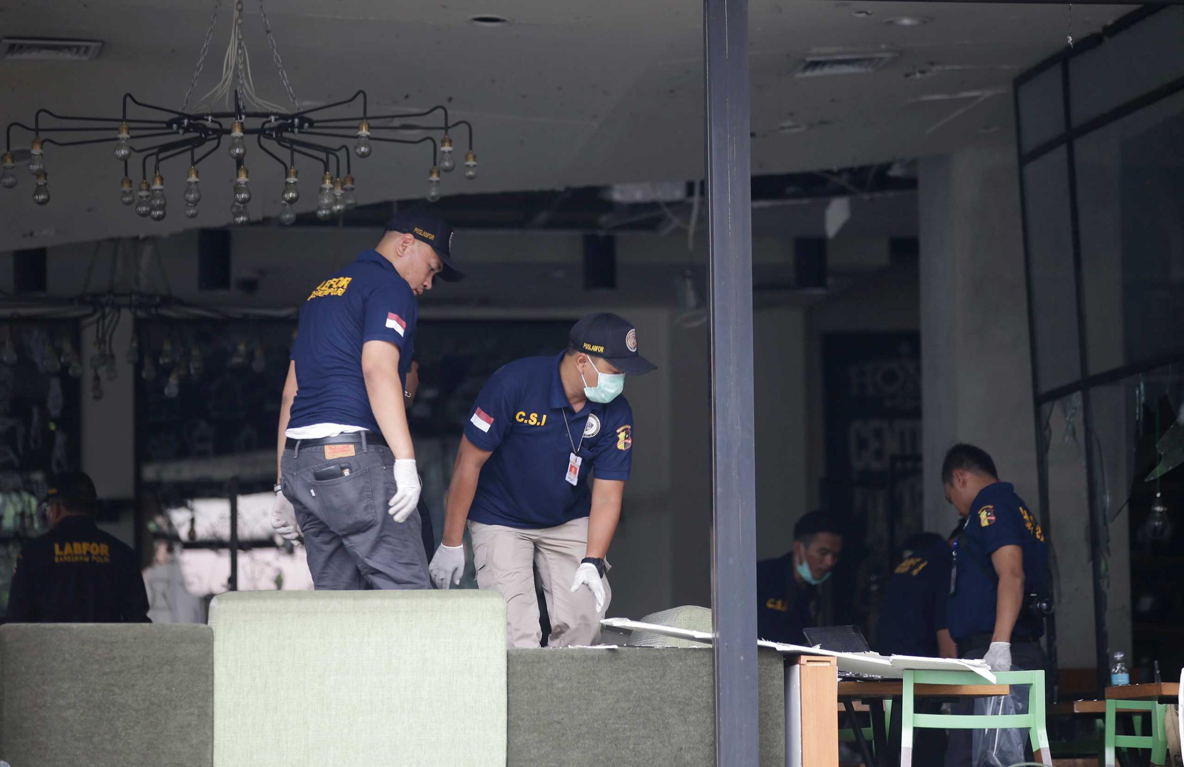 Police officers examine a damaged Starbucks café after an attack in Jakarta, Indonesia, Jan. 14, 2016.